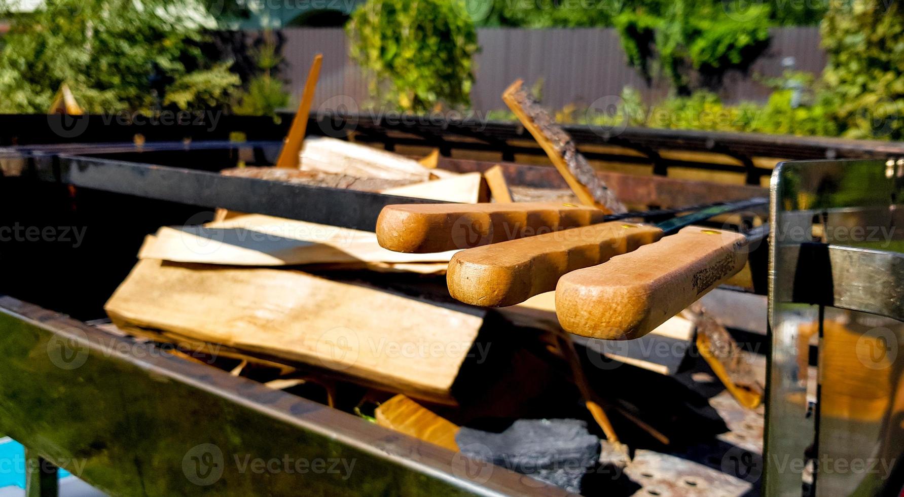 Firewood in a large stationary barbecue in the backyard of the house, barbecue area. Preparation for cooking meat and vegetables on the grill. Summer picnic with family on a green lawn photo