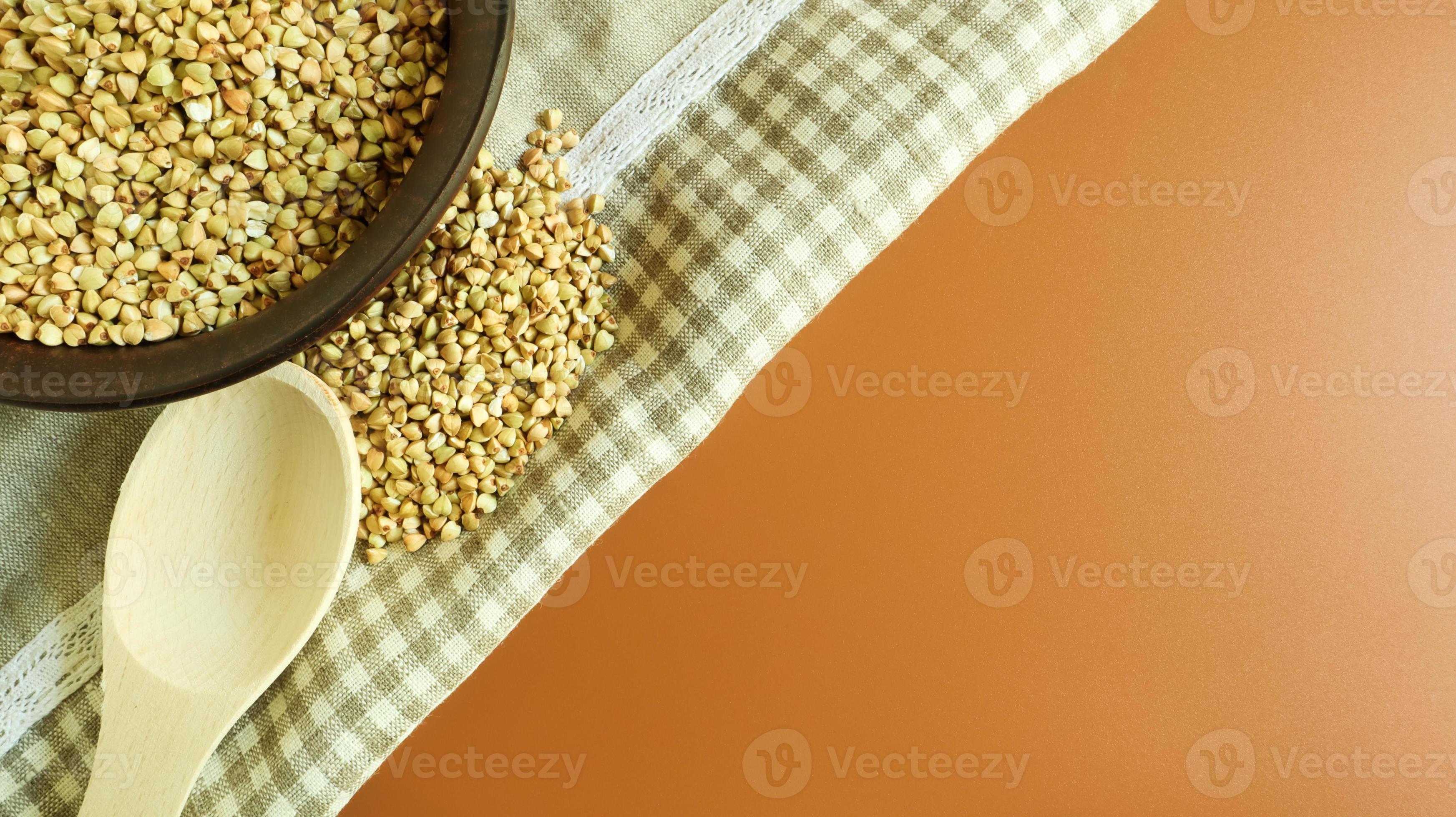 Raw green buckwheat in a brown clay plate and a wooden spoon. Vegan