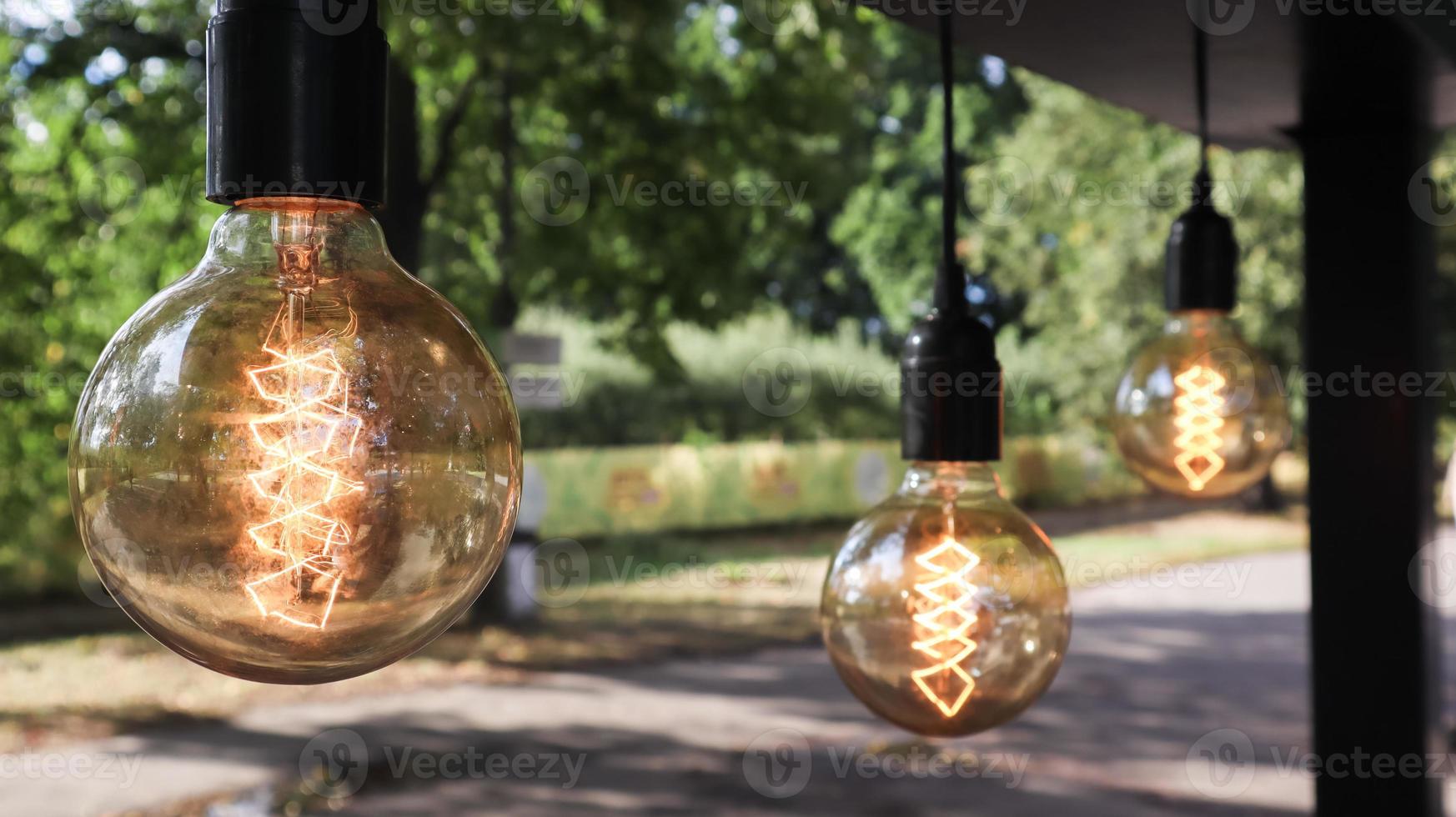 las bombillas incandescentes edison cuelgan en un estilo loft retro. primer plano de la decoración de la cafetería. decoración de la calle farolillos de luz luz cálida. enfoque suave, fondo de calle borroso foto