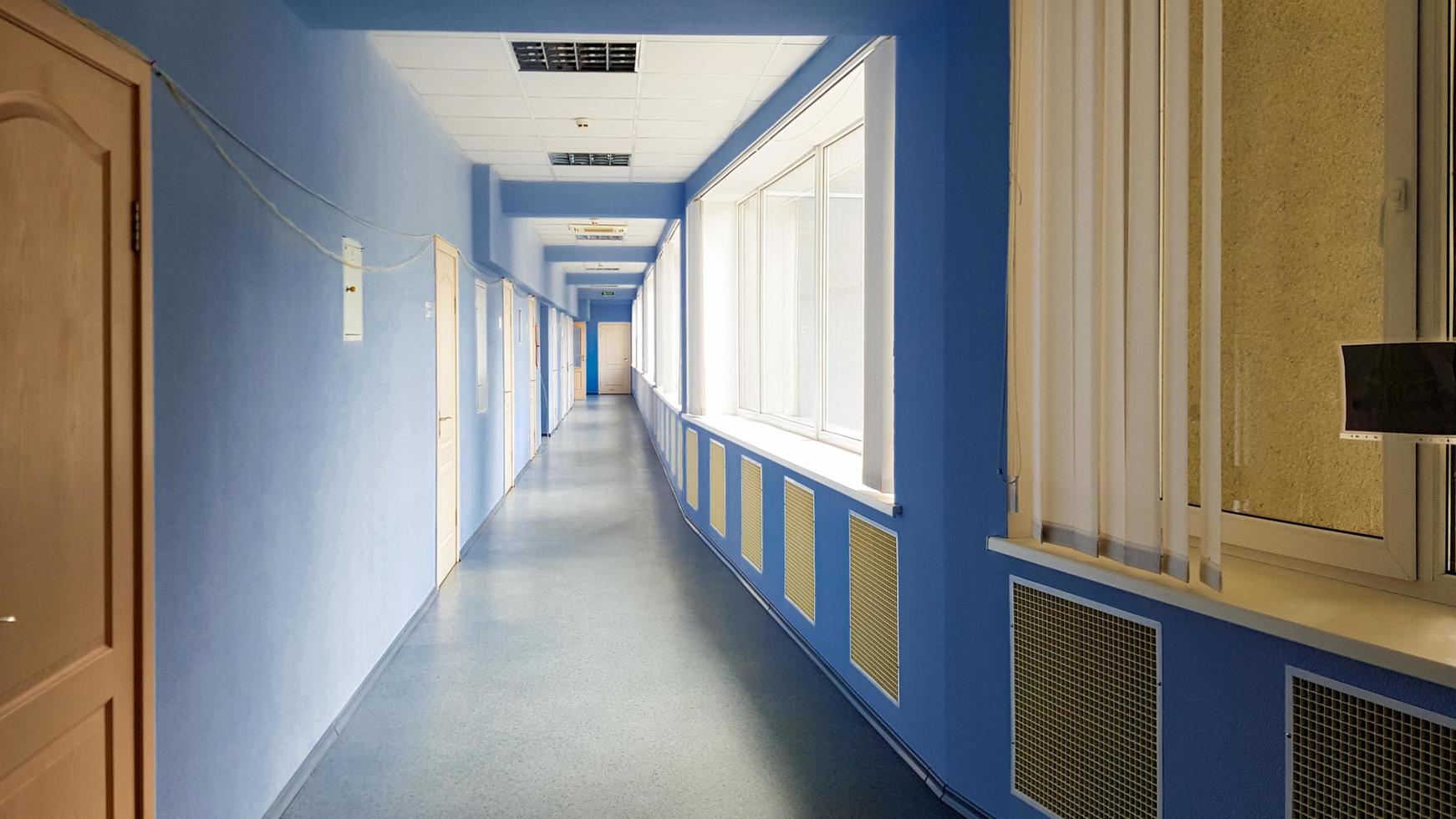 ucrania, kiev - 24 de septiembre de 2019. largo pasillo vacío sin gente en un hospital con paredes azules, puertas y ventanas de madera. los rayos del sol de las ventanas en un largo pasillo de color azul. foto