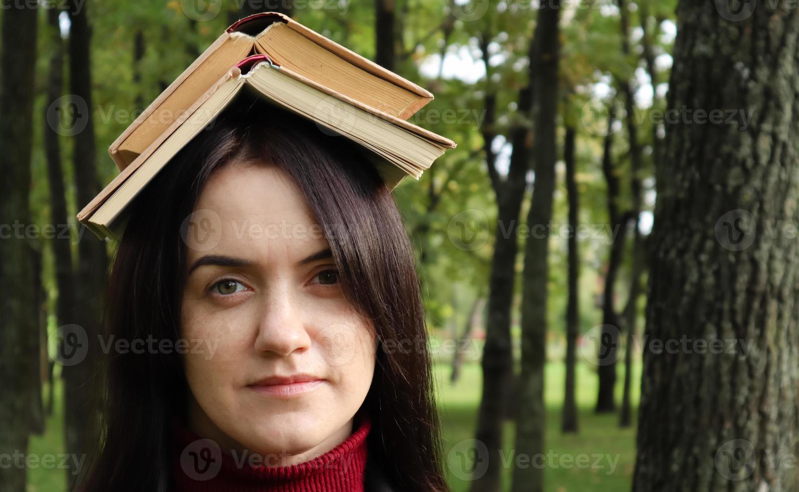 retrato de una morena joven y divertida en el parque con un libro abierto en la cabeza. aprender es divertido. mujer balanceándose con libros en la cabeza. el estudiante está cansado de leer. foto