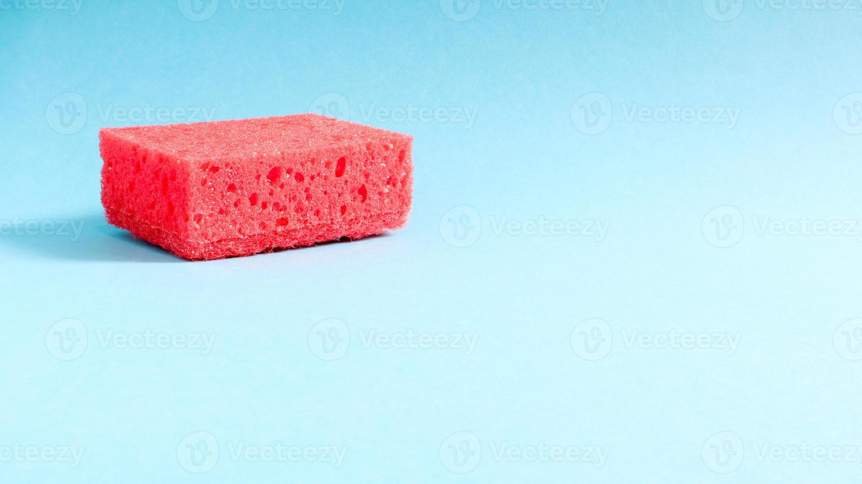 One red sponge on a blue background is used to wash and erase the dirt used by housewives in everyday life. They are made of porous material. Saving detergent, which allows you to use it sparingly photo
