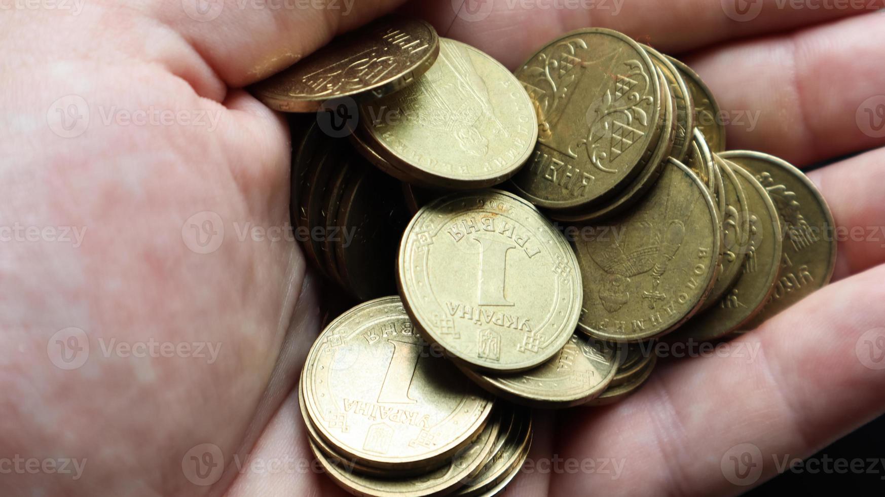 Ukrainian metal coins with a face value of 1 hryvnia in the palm of a male hand. A handful or pile of coins in the hands. Concept of retirement, savings and wealth, credit and mortgage, poverty. photo