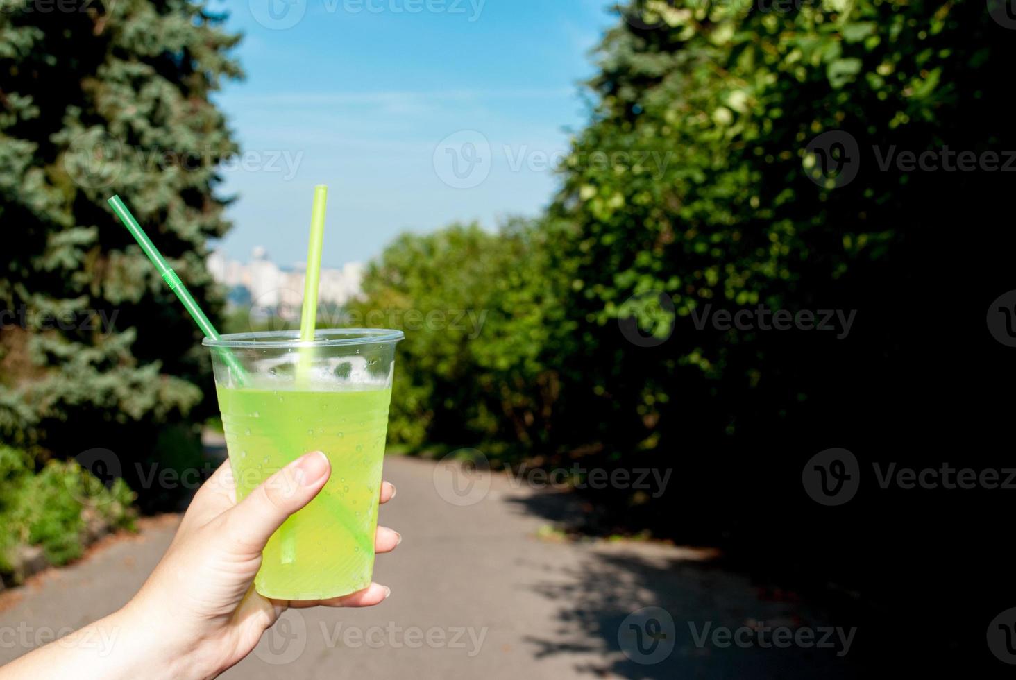 mujer sosteniendo una copa de cóctel verde de plástico cerca, al aire libre en verano en el parque foto