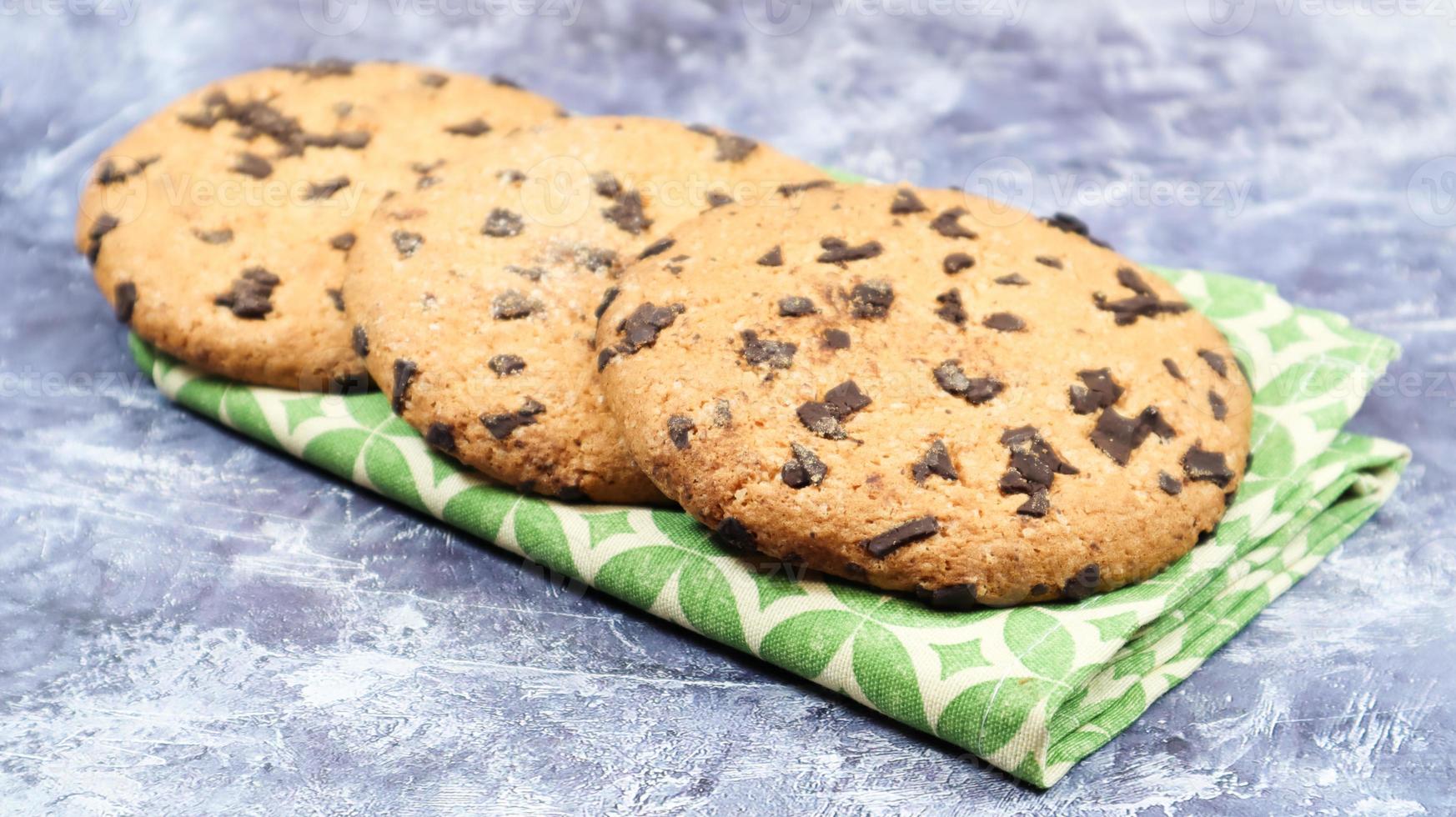 American chocolate chip cookies on a green napkin on a gray background. Traditional round crispy dough with chocolate chips. Bakery. Delicious dessert, pastries. photo