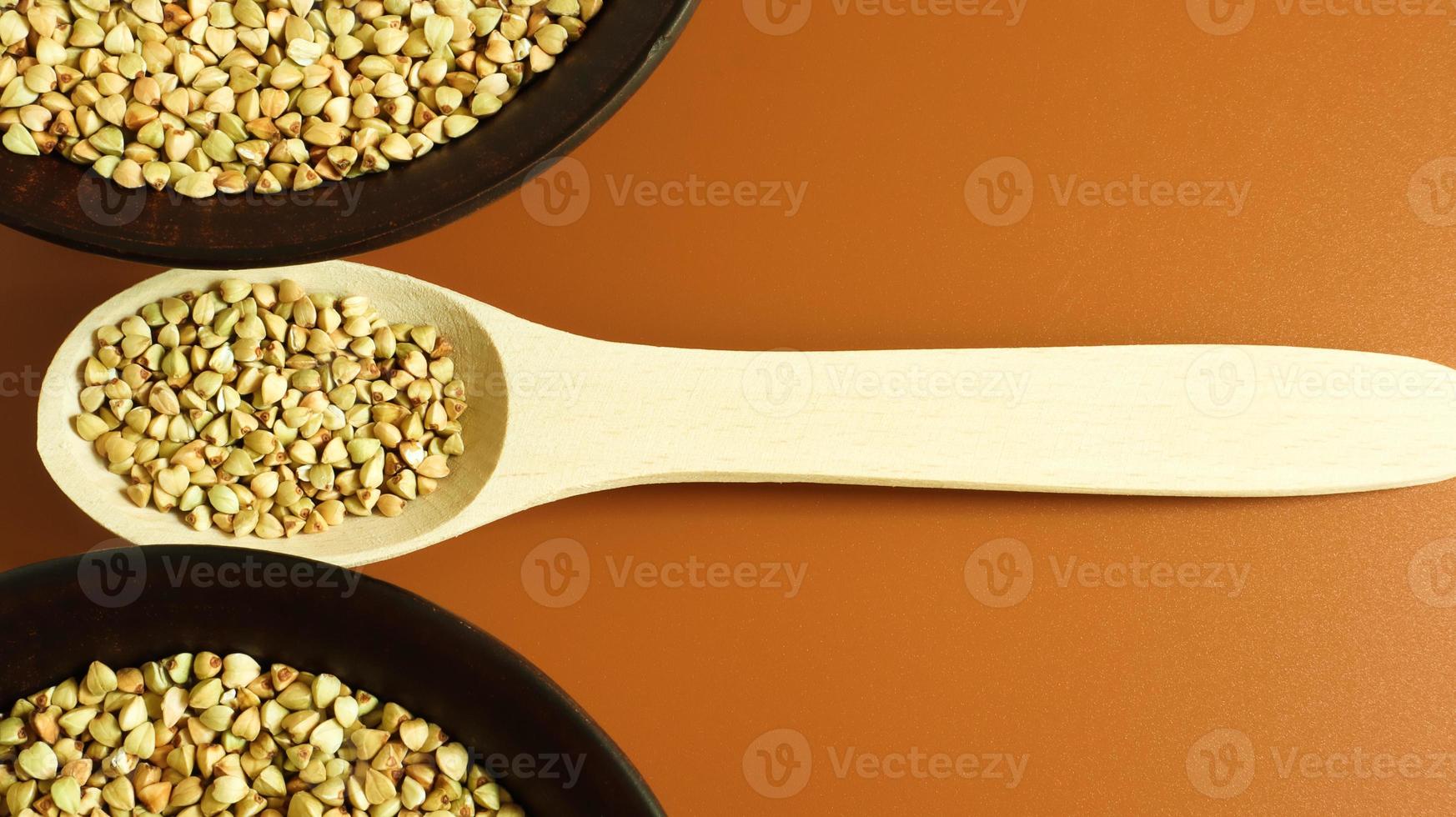 Raw green buckwheat in a brown clay plate and a wooden spoon. Vegan organic food concept. The concept of diet, weight loss, healthy and proper nutrition. Copy space for text. Top view, flat lay photo