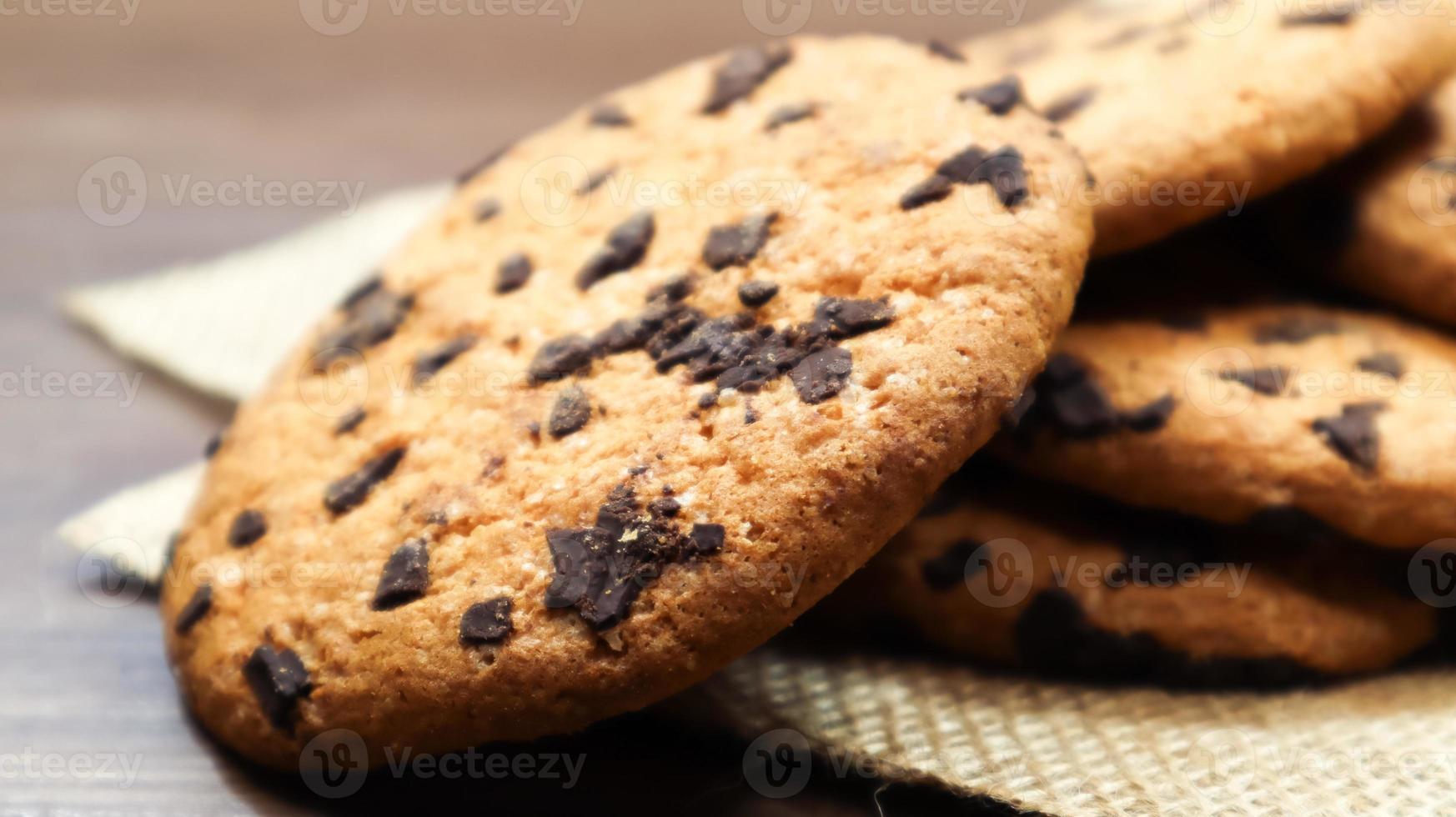 American chocolate chip cookies on a brown wooden table and on a linen napkin close-up. Traditional rounded crunchy dough with chocolate chips. Bakery. Delicious dessert, pastries. Rural still life. photo