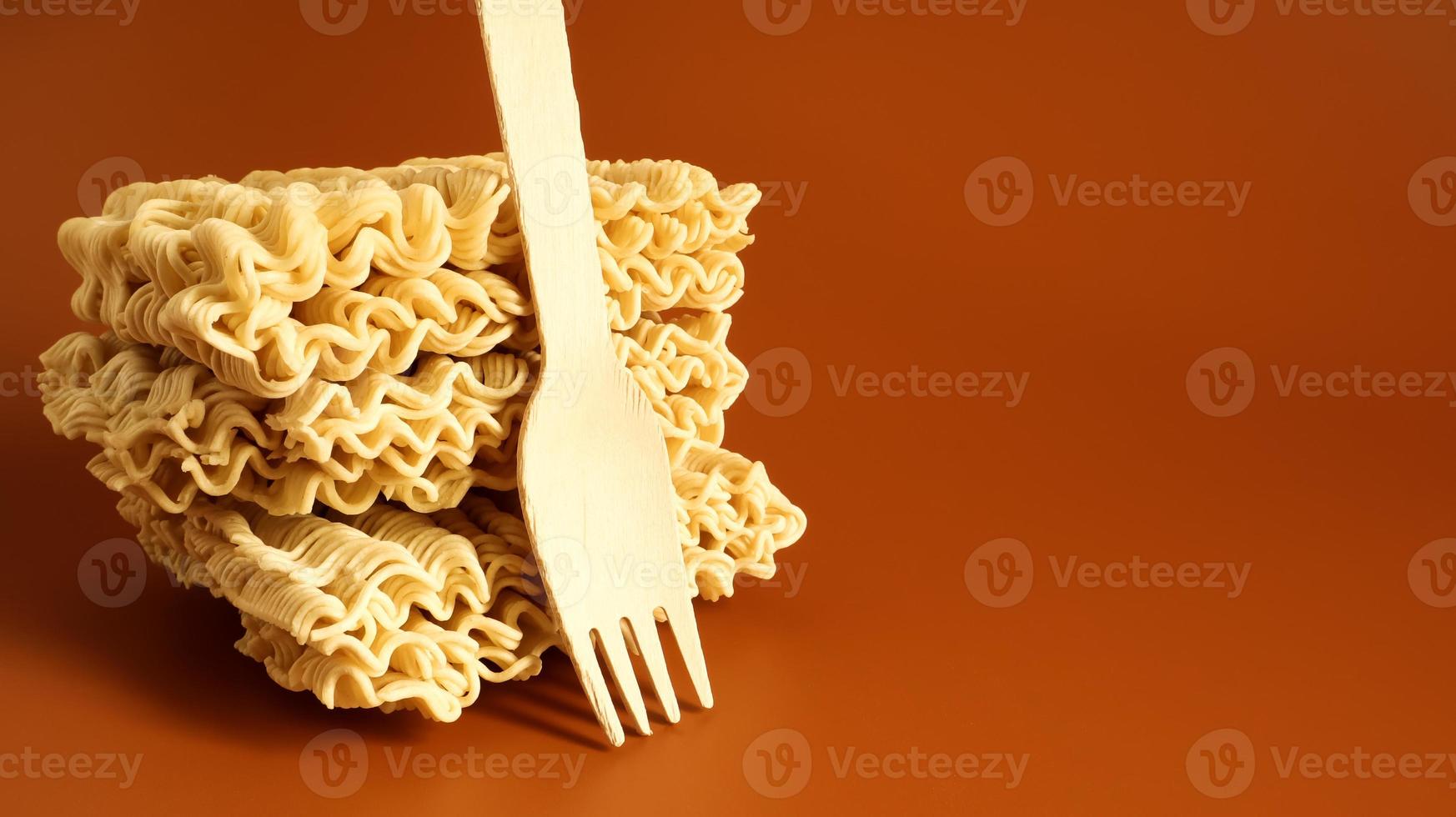 Raw square-shaped instant noodles with a wooden fork, stacked in a stack of three servings. pasta, for the preparation of which it is enough to pour boiling water and wait a few minutes. Copy space photo
