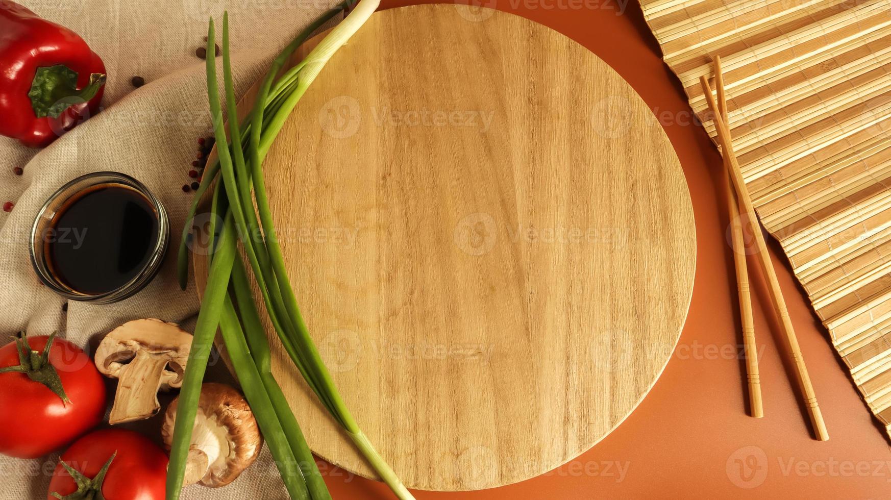 Round wooden board, sauce and various vegetables on the table, wooden stick on a brown background. Flat lay. Copy space in the center of the frame for your text or logo. Recipe and Cooking photo