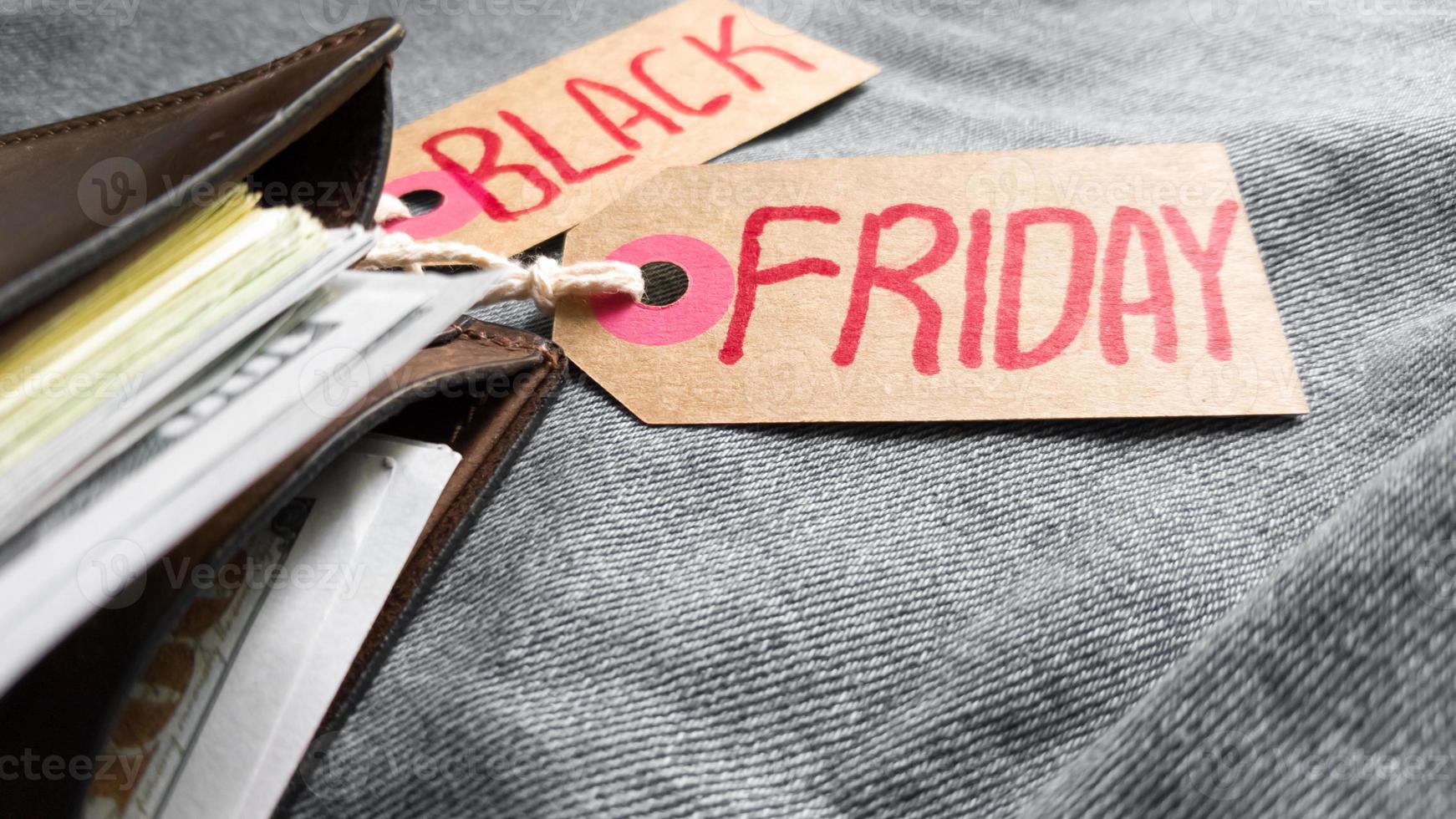 Brown wallet with money, dollars on a blue background, jeans texture, cardboard tag with red text Black Friday. Black Friday - International day of purchases, promotions, discounts, sales. photo