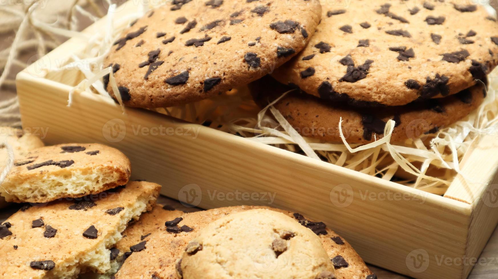 American chocolate chip cookies on a brown wooden table close-up in a box. Traditional rounded crunchy dough with chocolate chips. Bakery. Delicious dessert, pastries. Rural still life. photo