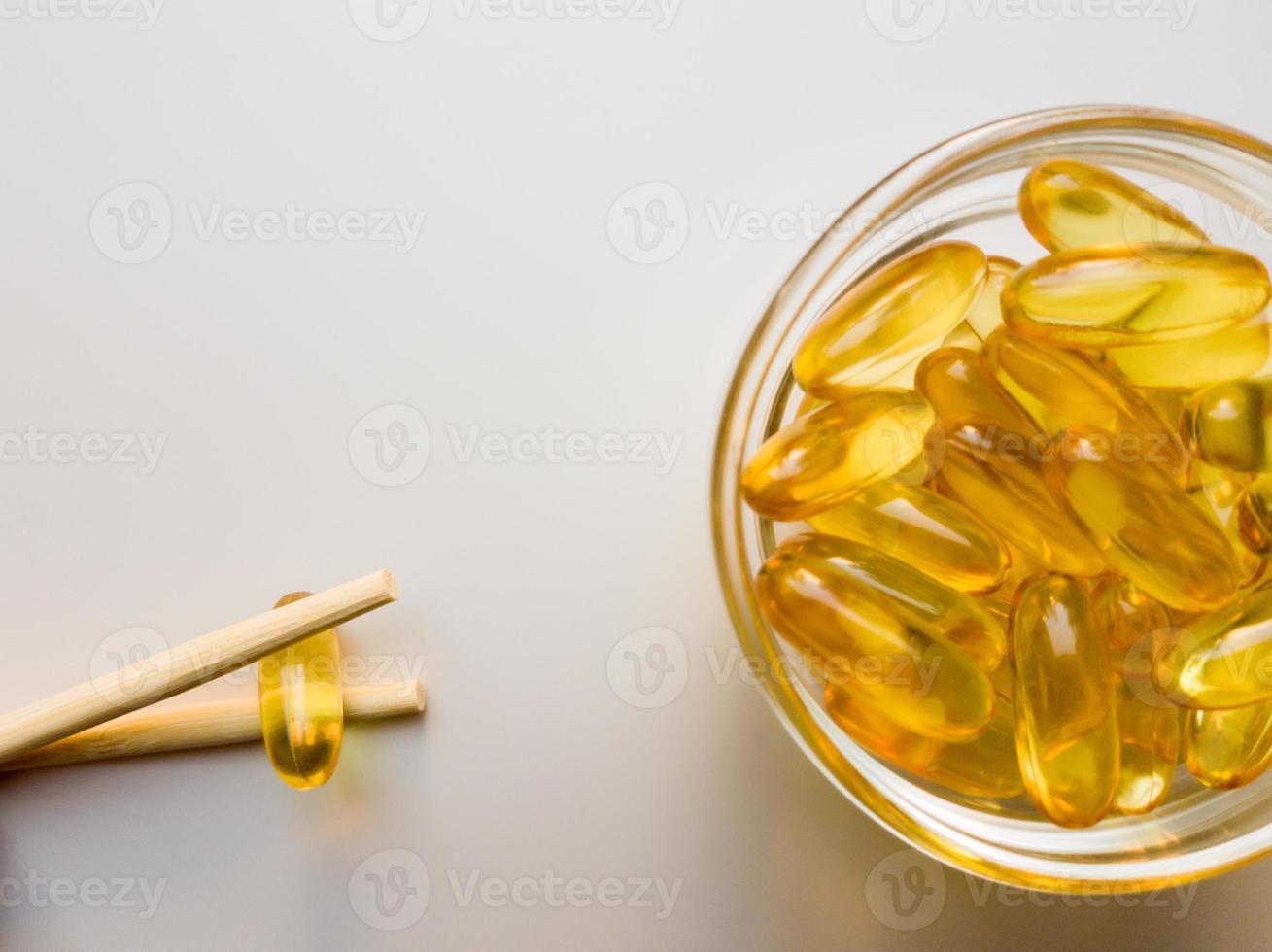 Fish oil capsules on a saucer with chopsticks. Bunch of vitamin omega 3 pills on a white background. Close-up, top view, high resolution product. Metabolism in the body. Body calcium. photo