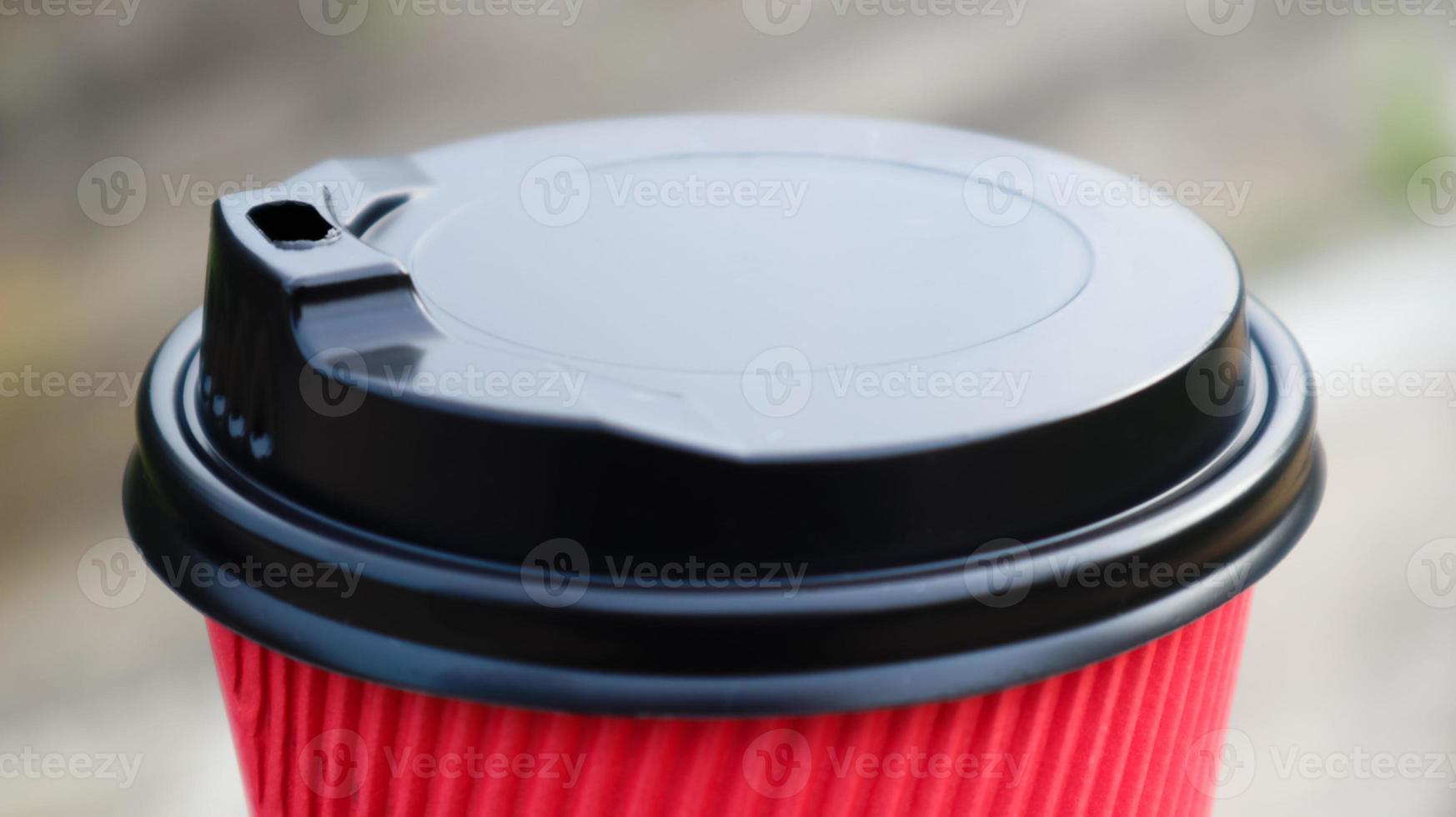 Coffee in a paper disposable eco glass of red color with a black plastic lid against the background of a city street. Selective focus. Close-up of the object. photo