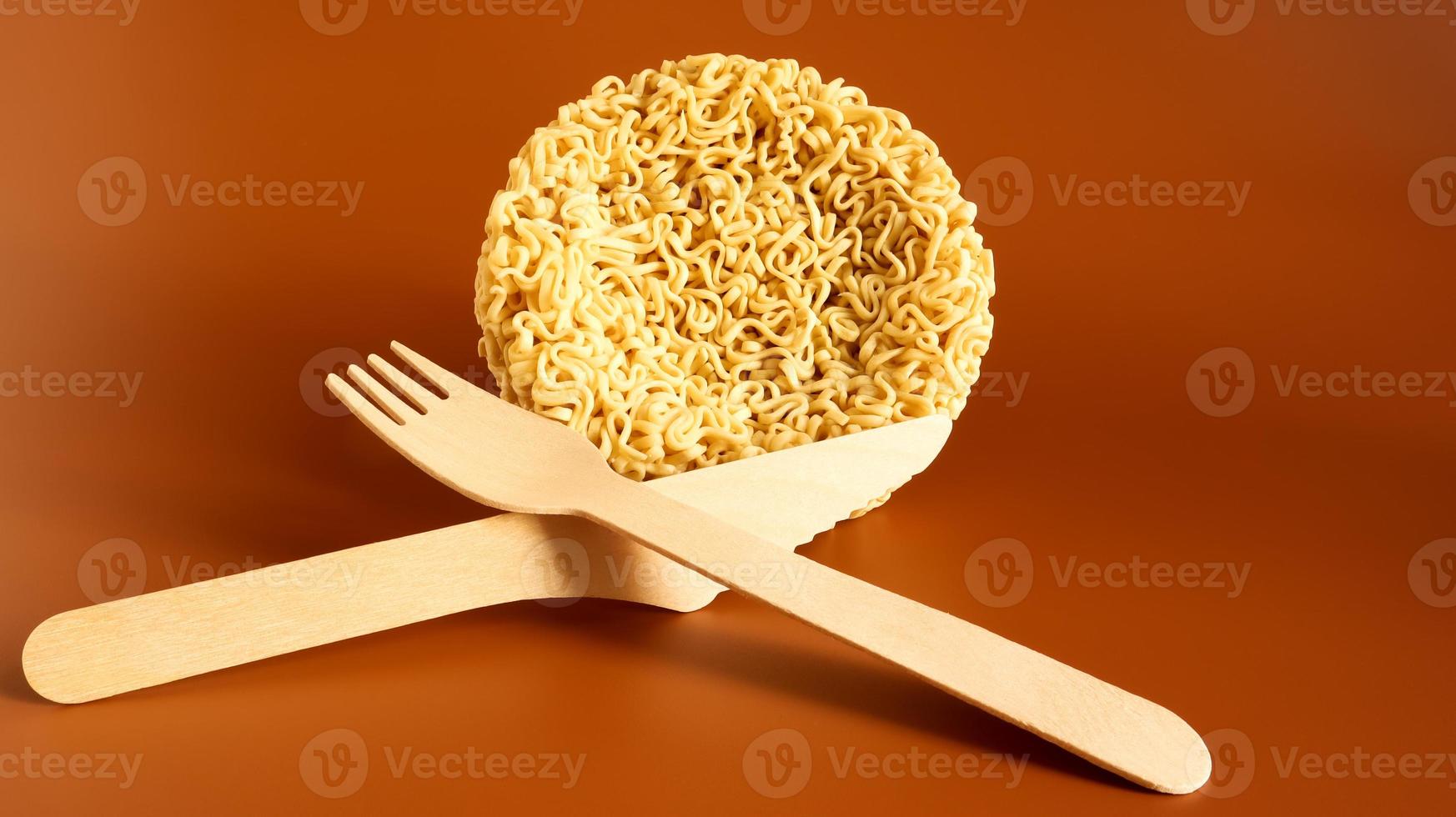 Raw instant noodles in the shape of a circle with a wooden disposable fork. pasta, for the preparation of which it is enough to pour boiling water and wait a few minutes. spaghetti. Copy space photo