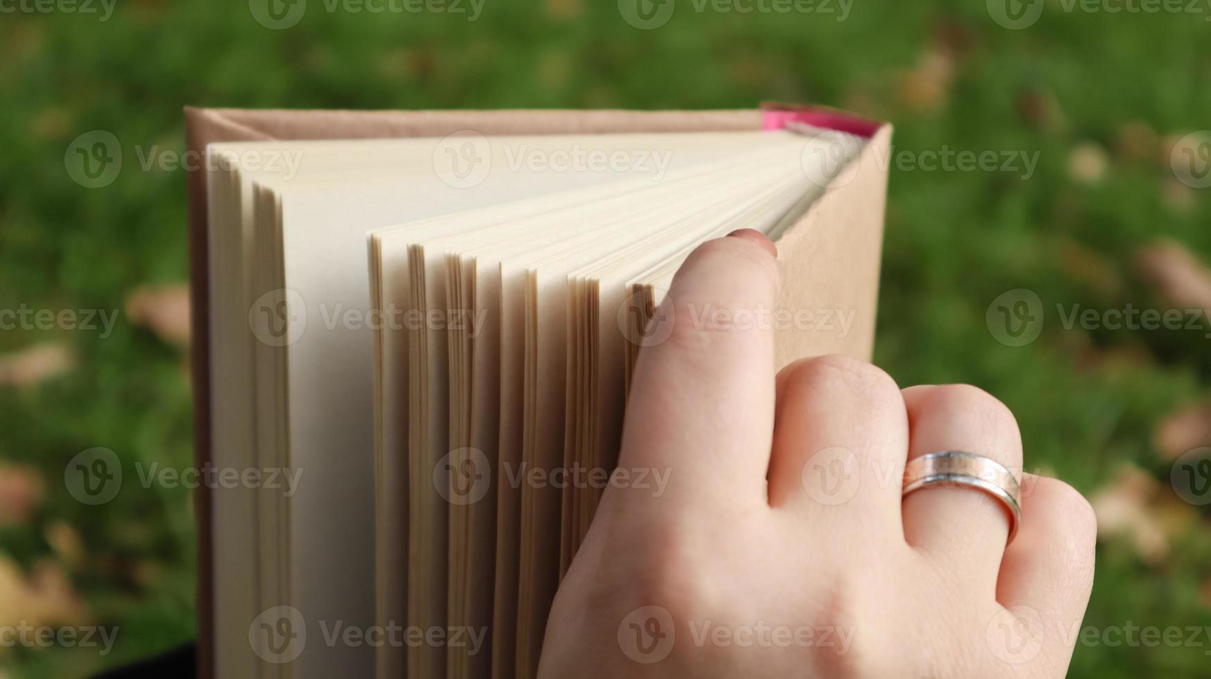 niña leyendo un libro en el parque de otoño. las manos femeninas abren las páginas de un libro de papel al aire libre en un día cálido y soleado. el estudiante se está preparando para el examen. ocio literario en la naturaleza. foto