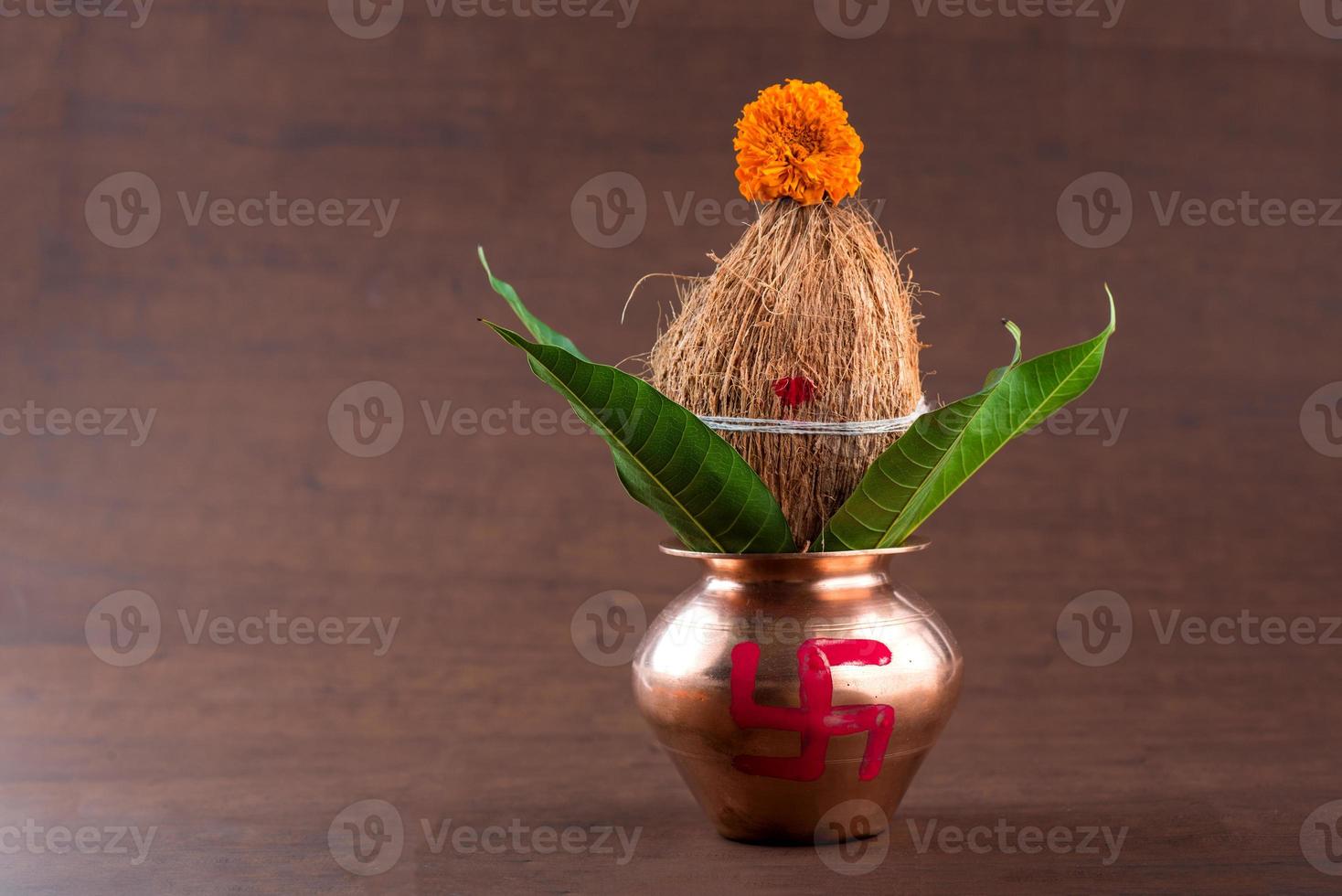 Copper kalash with coconut and mango leaf with floral decoration on a wooden background. essential in hindu puja. photo