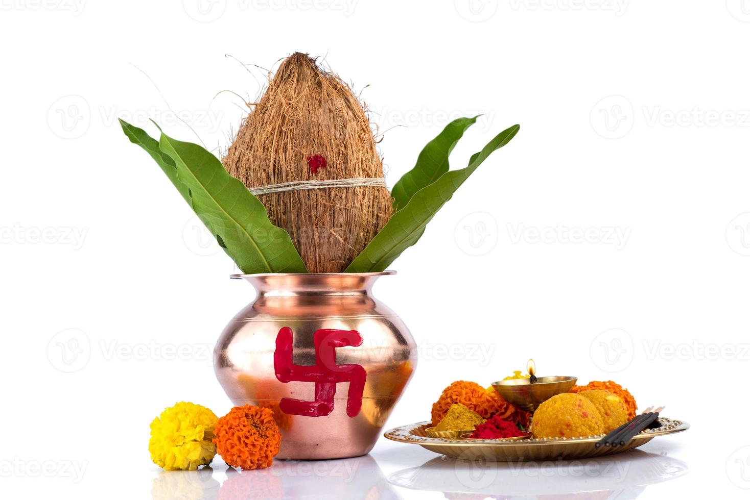 Copper Kalash with coconut and mango leaf and pooja thali with diya, kumkum and sweets with floral decoration on a white background. Essential in hindu puja. photo