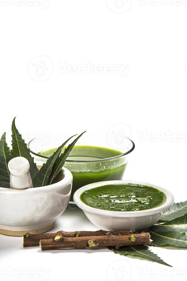 Medicinal Neem leaves in mortar and pestle with neem paste, juice and twigs on white background photo
