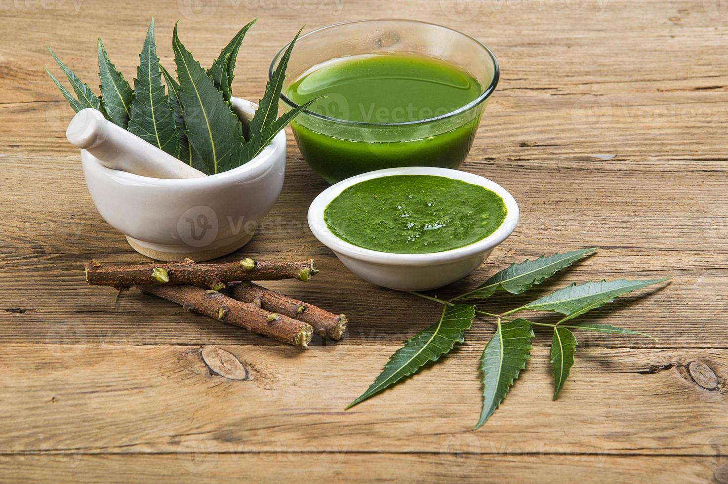 Medicinal Neem leaves in mortar and pestle with neem paste, juice and twigs on wooden background photo