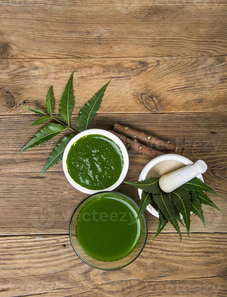 Medicinal Neem leaves in mortar and pestle with neem paste, juice and twigs on wooden background photo