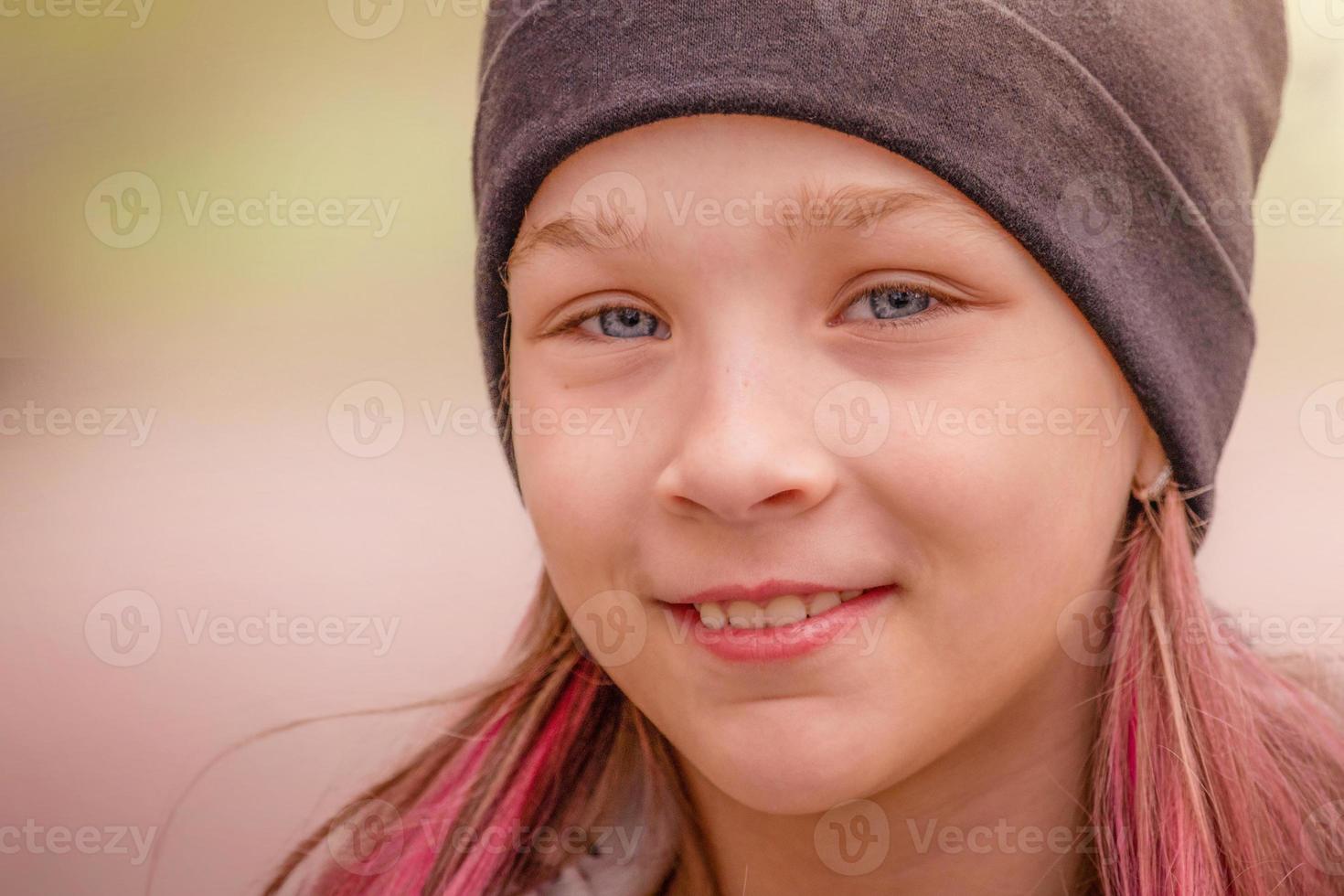 Girl with pink hair in a cap outdoors. The child smiles. photo