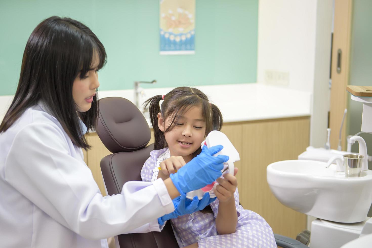 Female dentist demonstrating how to brush teeth to a little girl in dental clinic, teeth check-up and Healthy teeth concept photo