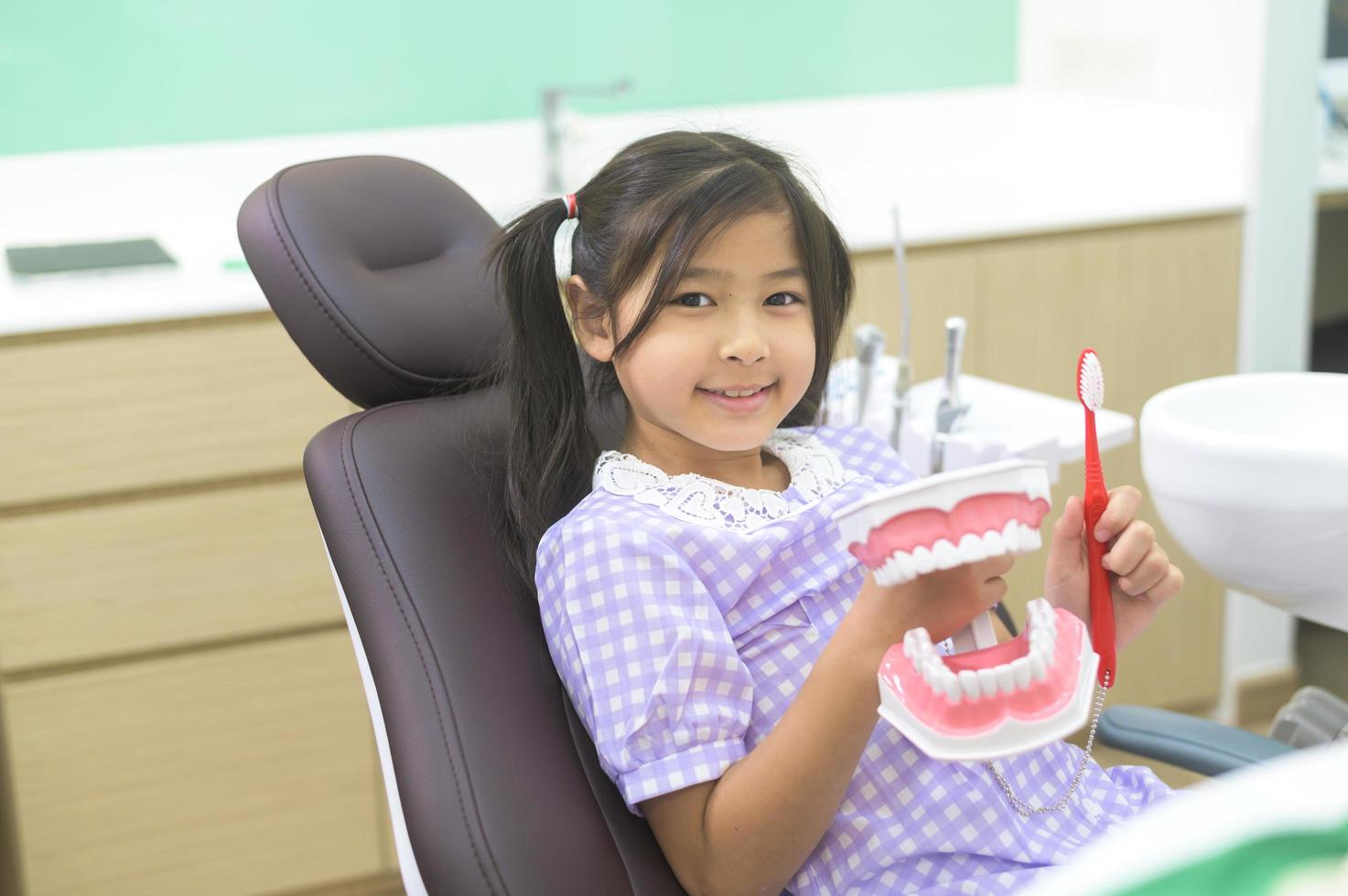 Female dentist demonstrating how to brush teeth to a little girl in dental clinic, teeth check-up and Healthy teeth concept photo