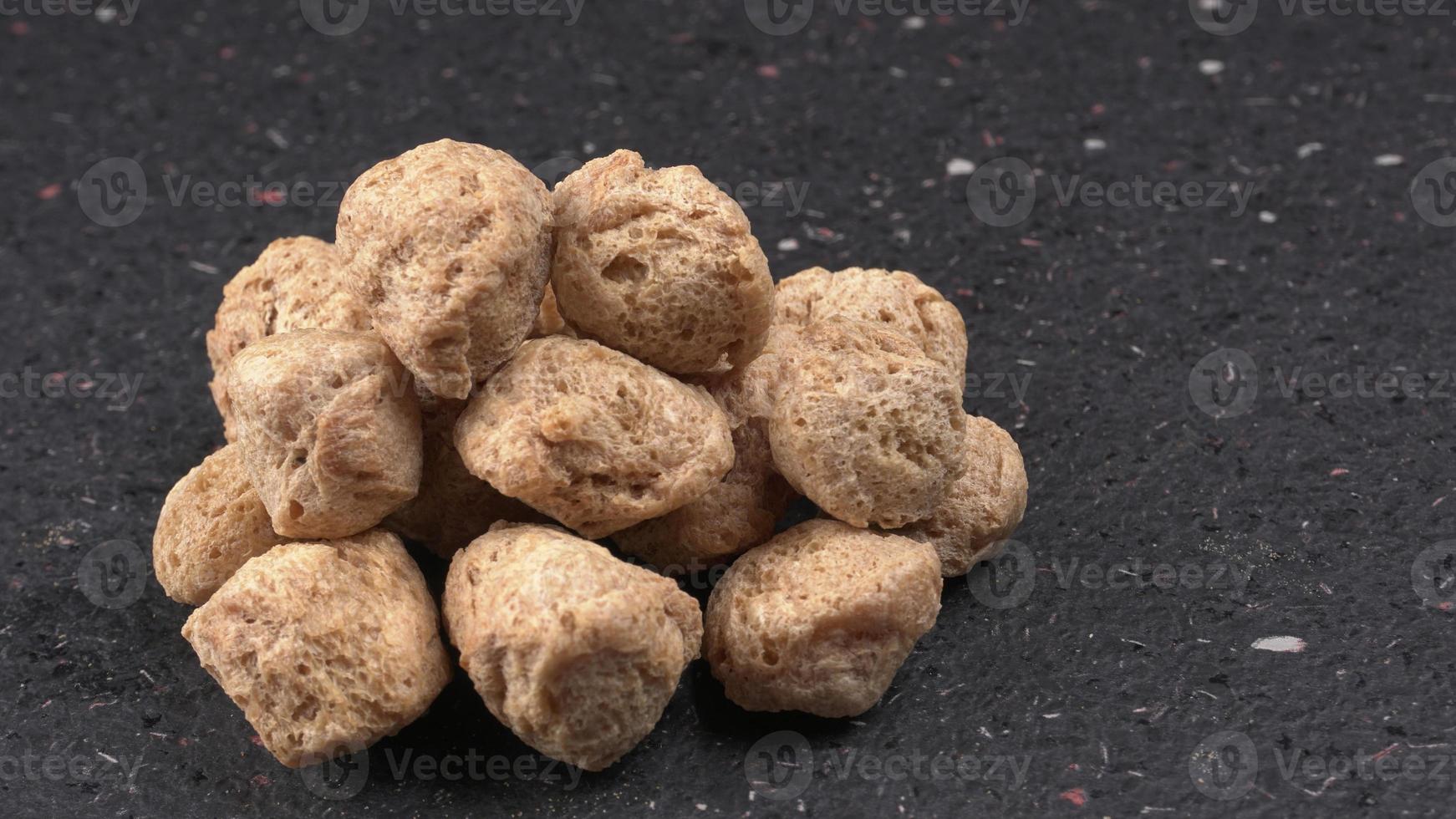 Raw soya chunks on dark background. Healthy, nutritious soybean meat, chunks isolated.Vegan food concept. photo