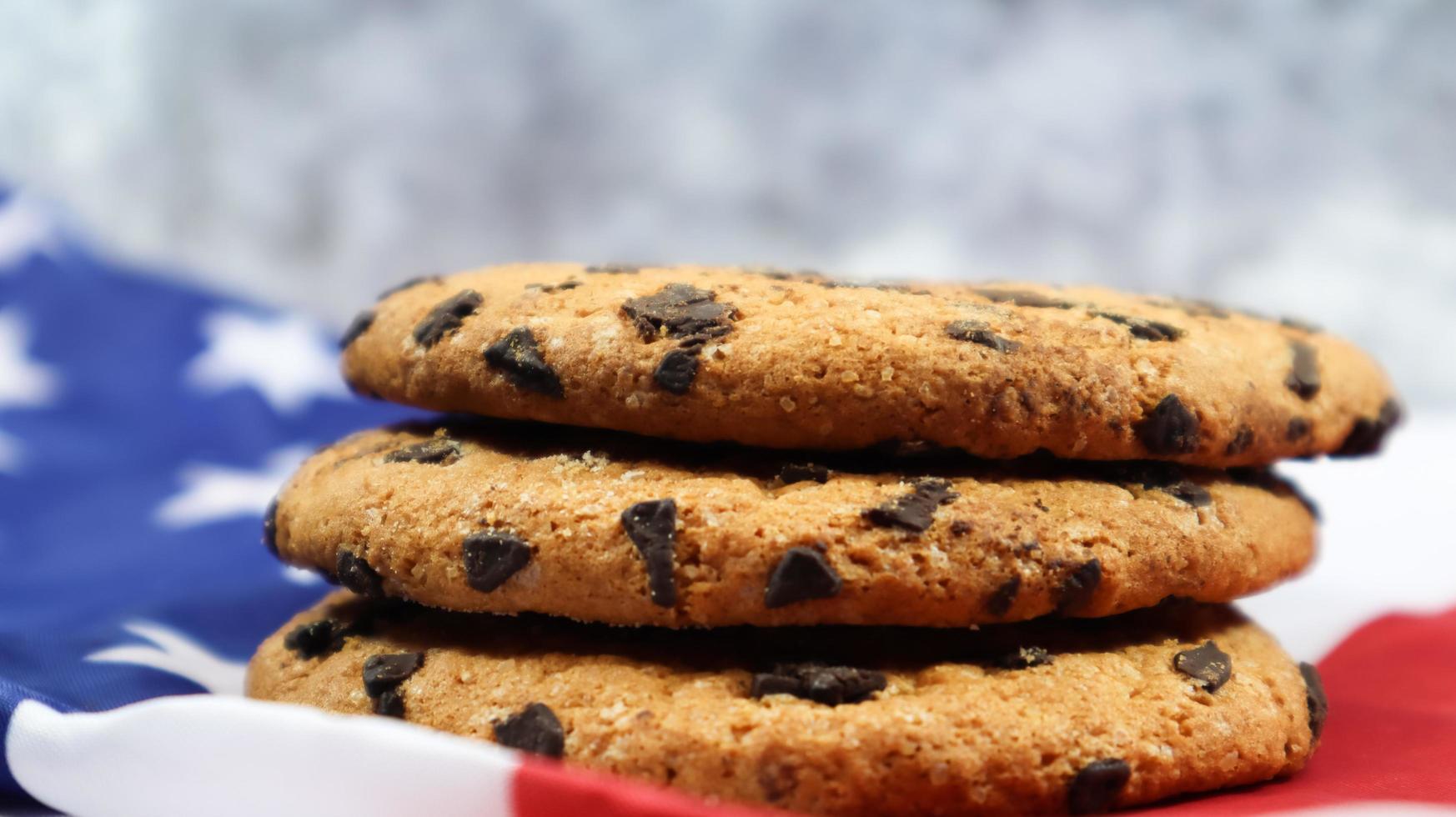 Patriotic cookies. Three rounded traditional chocolate chip cookies on the background of the flag of the United States of America. Delicious sweet pastries, dessert. America's favorite treat. photo
