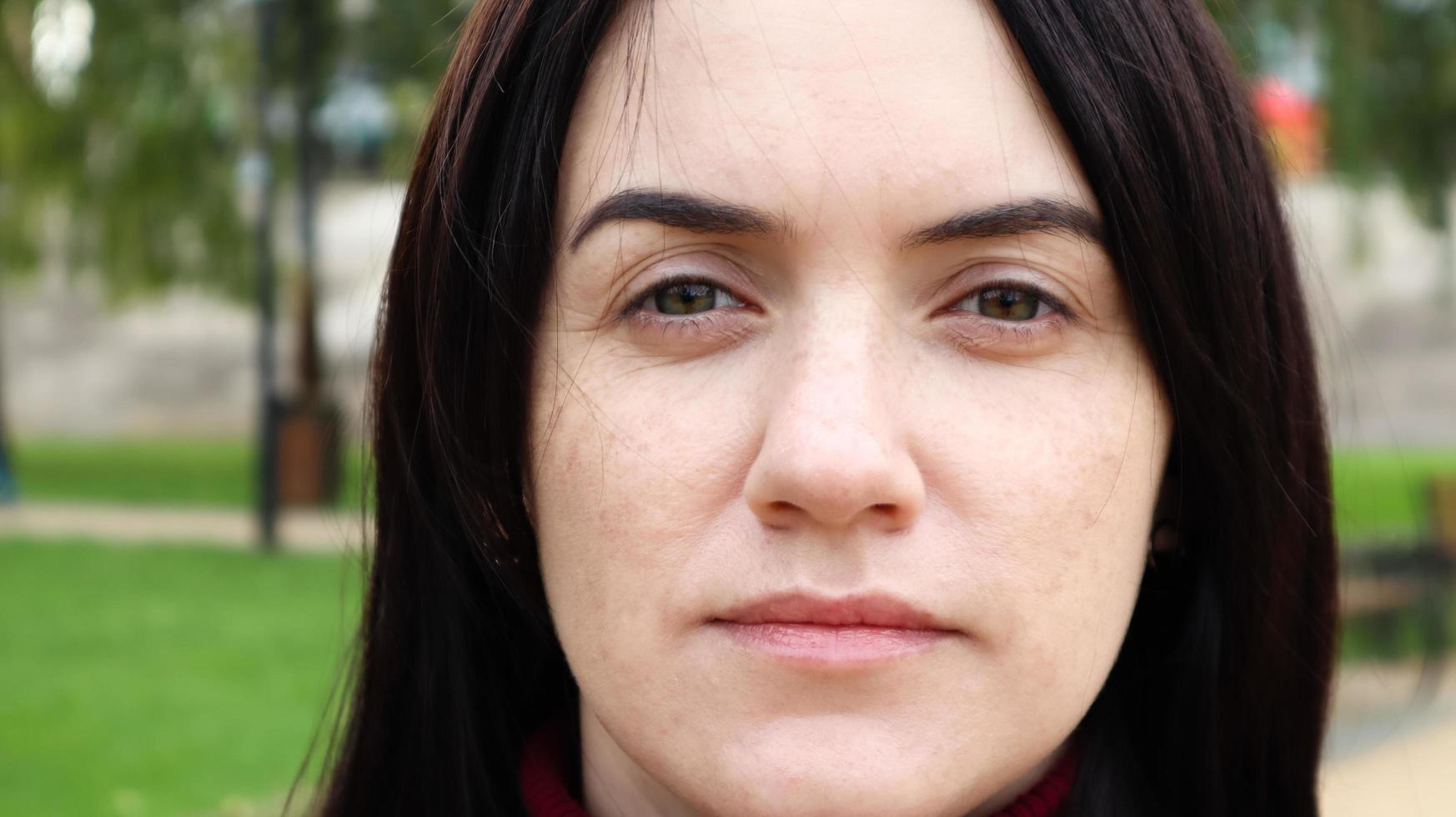 Close up portrait of beautiful caucasian woman while walking outdoors in city park with blurred background. A woman is looking at the camera on a sunny day. photo