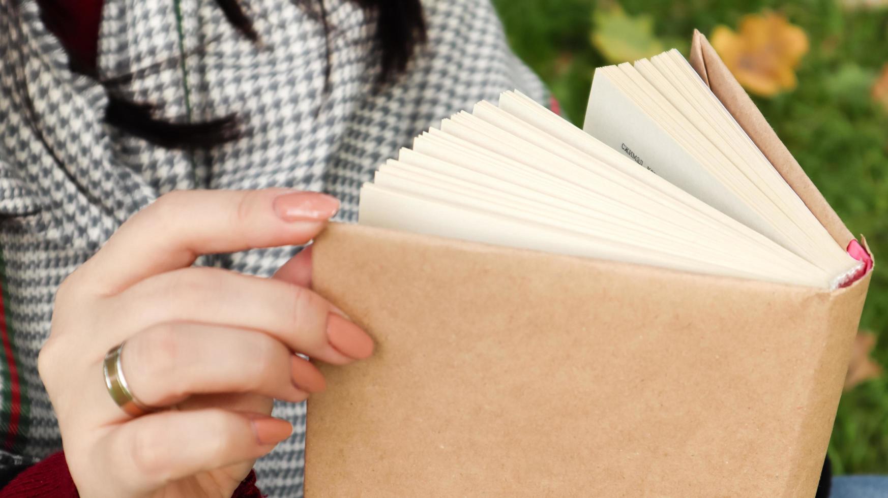 Girl reading a book in the autumn park. Female hands open the pages of a paper book outdoors on a warm sunny day. The student is preparing for the exam. Literary leisure in nature. photo