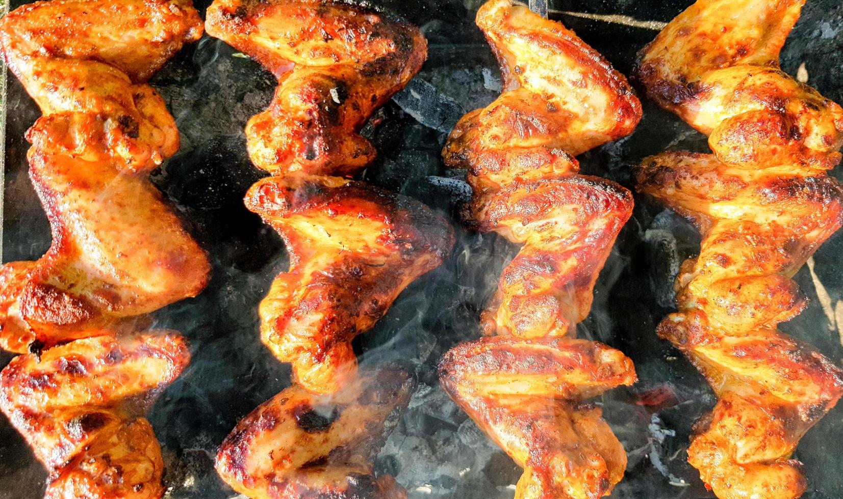 deliciosas alitas de pollo a la parrilla jugosas al aire libre en humo. proceso de cocción del pollo a la barbacoa foto