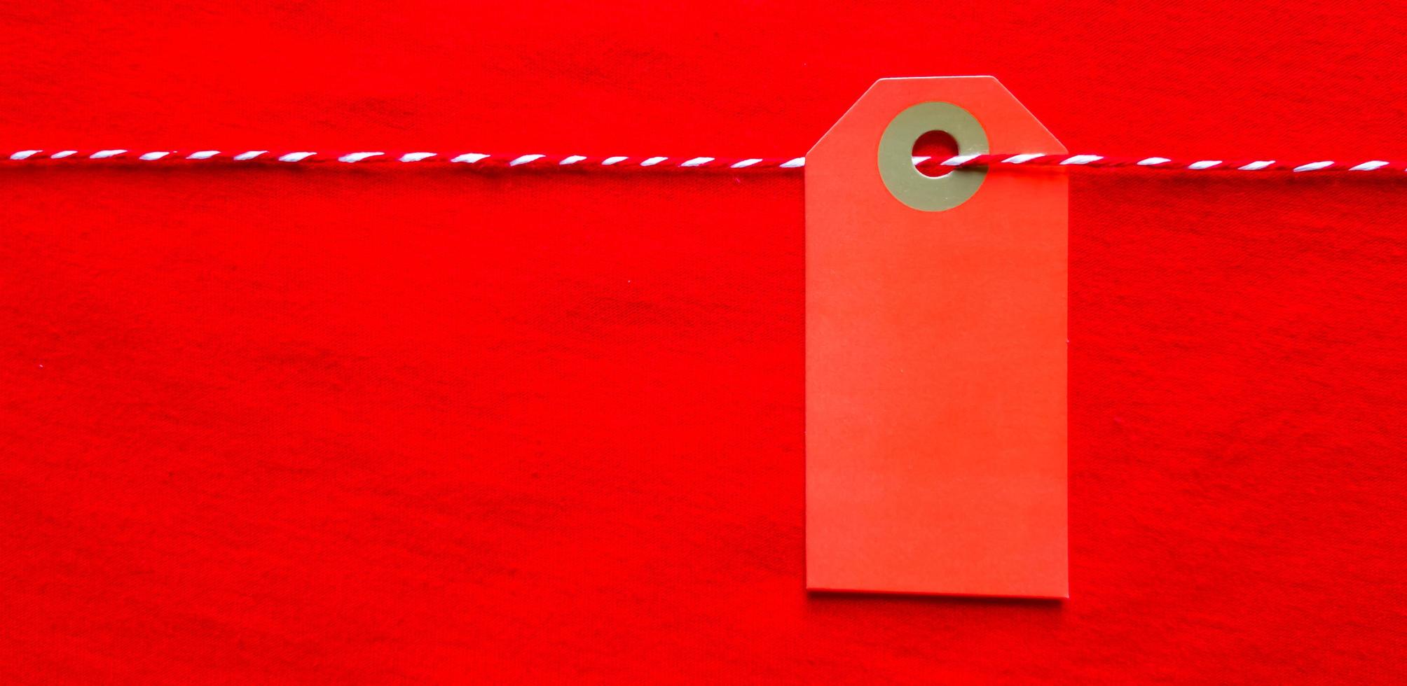 Red tag tag hanging on a red rope on a red background. Copy space, place for text, flat lay. photo