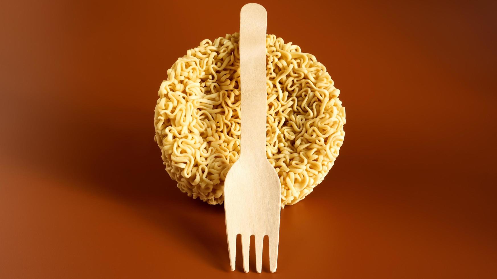 Raw instant noodles in the shape of a circle with a wooden disposable fork. pasta, for the preparation of which it is enough to pour boiling water and wait a few minutes. spaghetti. Copy space photo