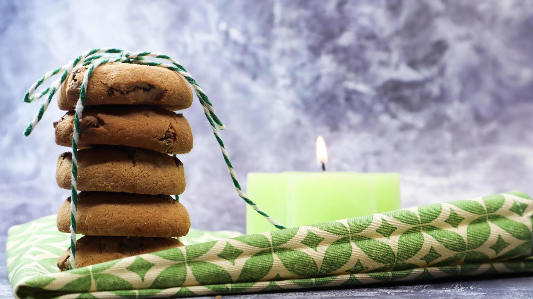 American chocolate chip cookies in a stack tied with thread on a green napkin and a candle. Traditional rounded crunchy dough with chocolate chips. Bakery. Delicious dessert, pastries. photo