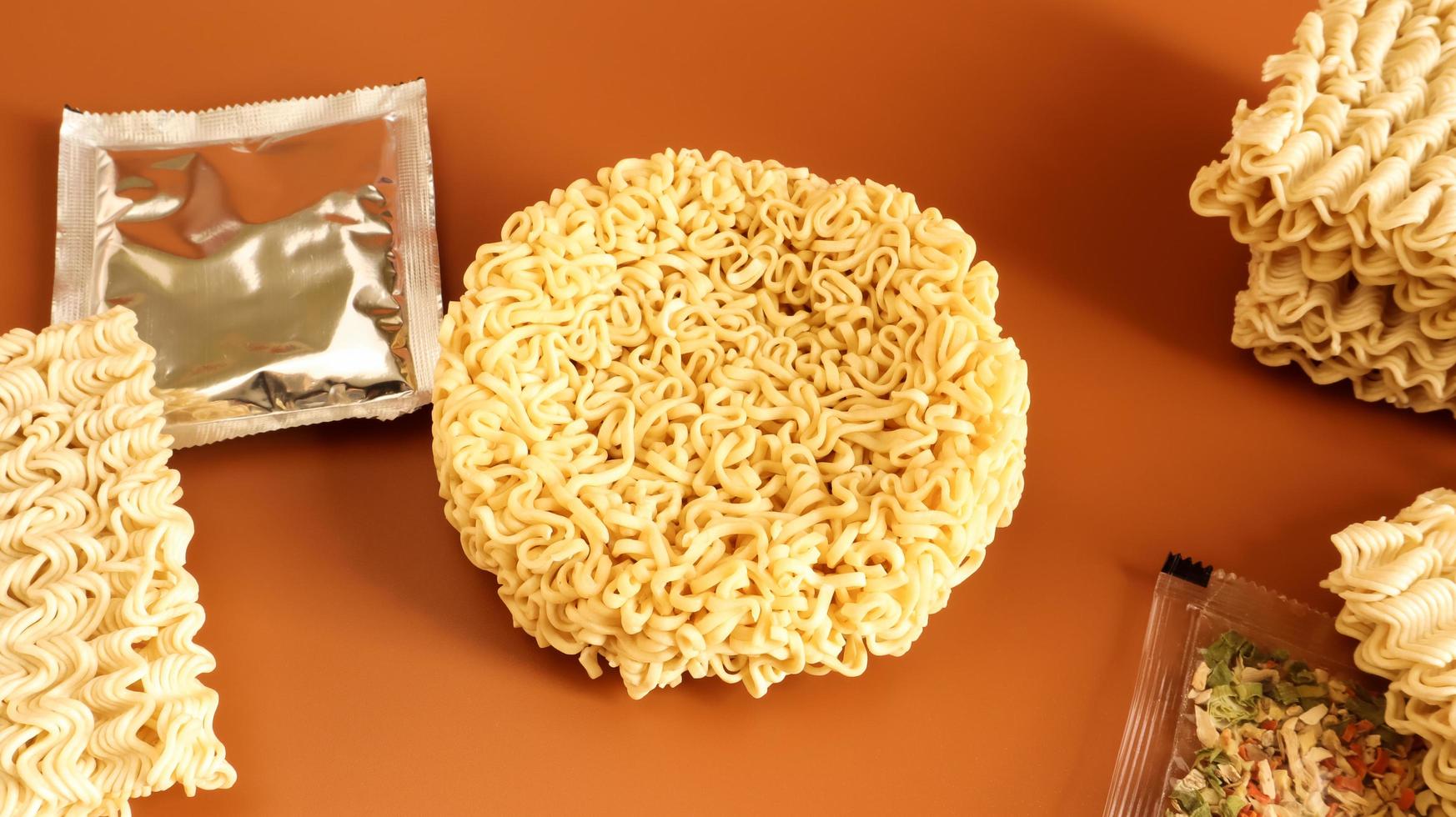 circle of instant noodles with raw spices on a plain brown background. Sprinkle dry Chinese or Korean vermicelli with salt and spices before pouring boiling water. pasta and flavors included photo