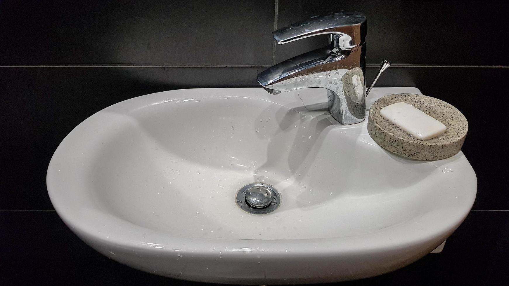 Bathroom interior with sink and faucet. Modern apartment in the attic of the house. White ceramic washbasin with chrome tap on a black tile wall photo