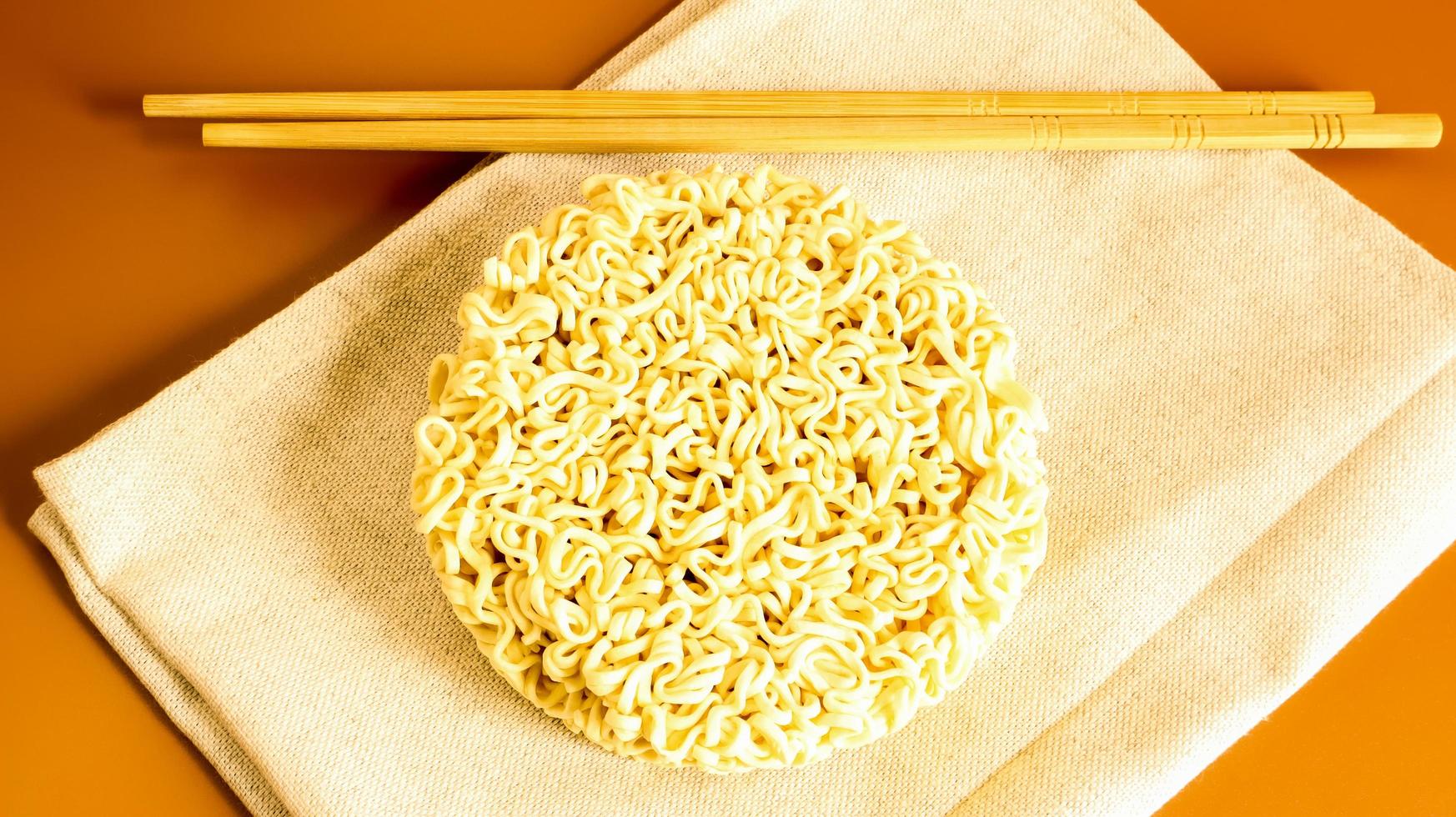 raw instant noodles on a towel with chopsticks on a yellow background. pasta, for the preparation of which it is enough to pour boiling water over it and wait a few minutes. Copy space. photo