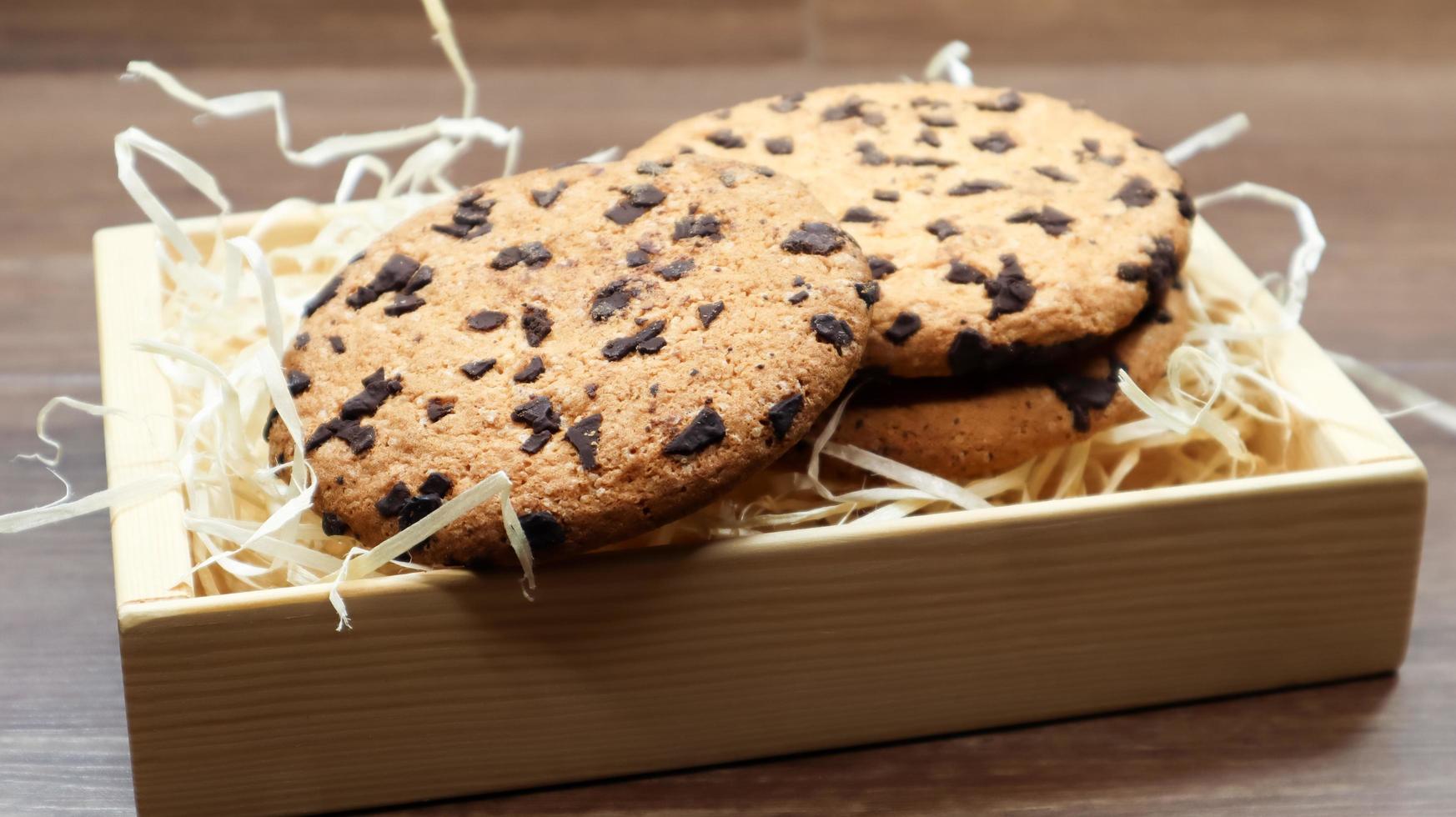 American chocolate chip cookies on a brown wooden table close-up in a box. Traditional rounded crunchy dough with chocolate chips. Bakery. Delicious dessert, pastries. Rural still life. photo