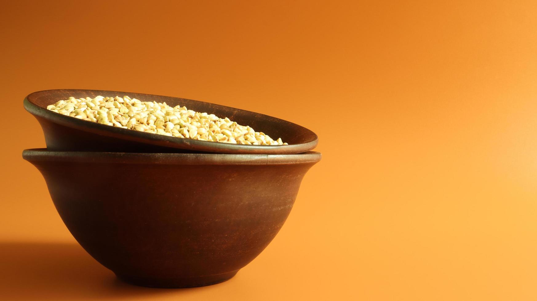 Raw green buckwheat in a brown clay plate on a brown background. Vegan organic food concept. The concept of diet, weight loss, healthy and proper nutrition. Copy space for text or logo. photo