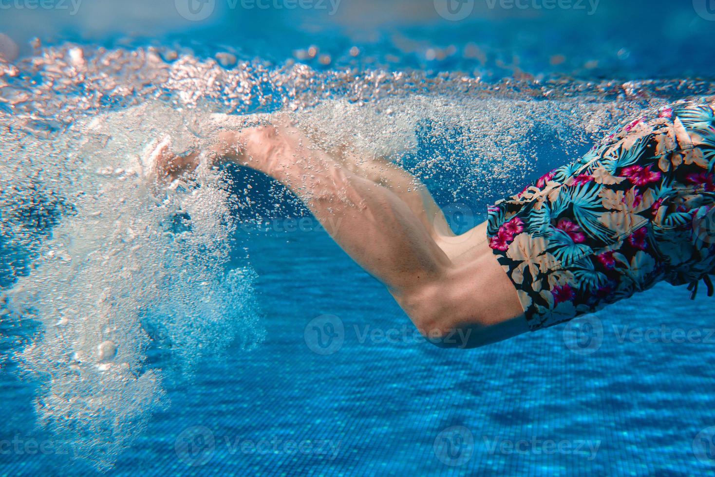 Men's legs swimming underwater in the swimming pool in summer photo