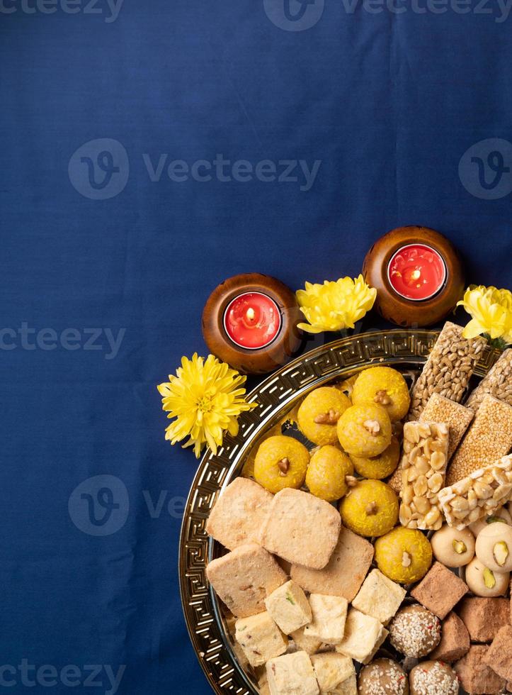 traditional indian sweets on blue background with candles and flowers flat lay photo