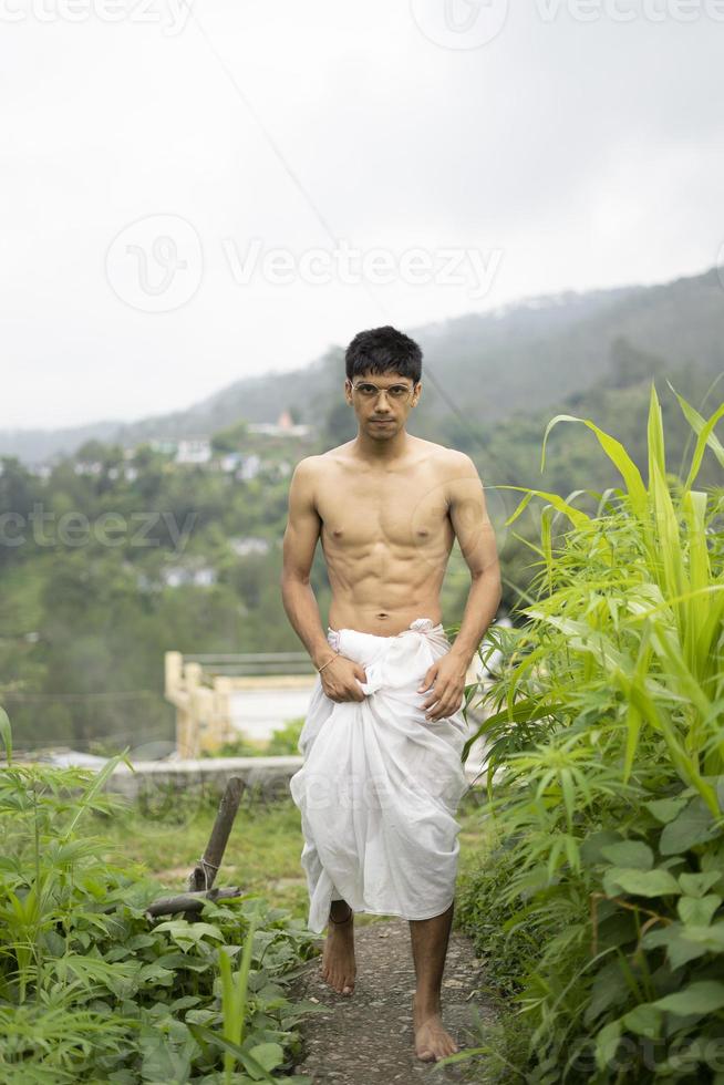 Young Indian fit boy, walking on a pathway beside crops in the field. An Indian priest walking while wearing white dhoti. Indian religious man. photo