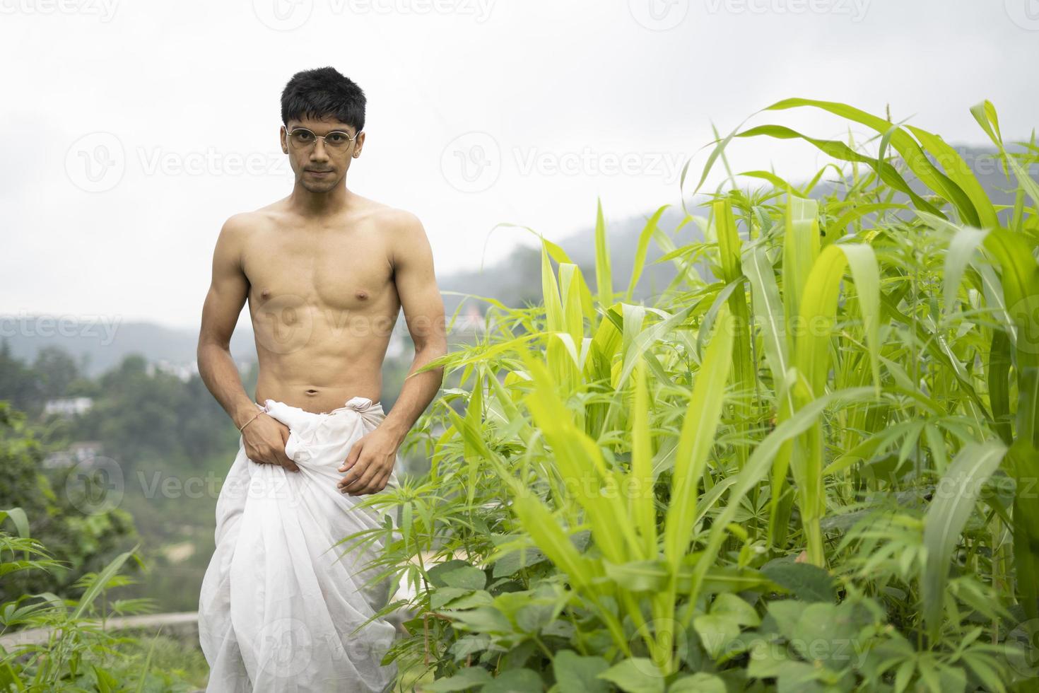 Young Indian fit boy, walking on a pathway beside crops in the field. An Indian priest walking while wearing white dhoti. Indian religious man. photo