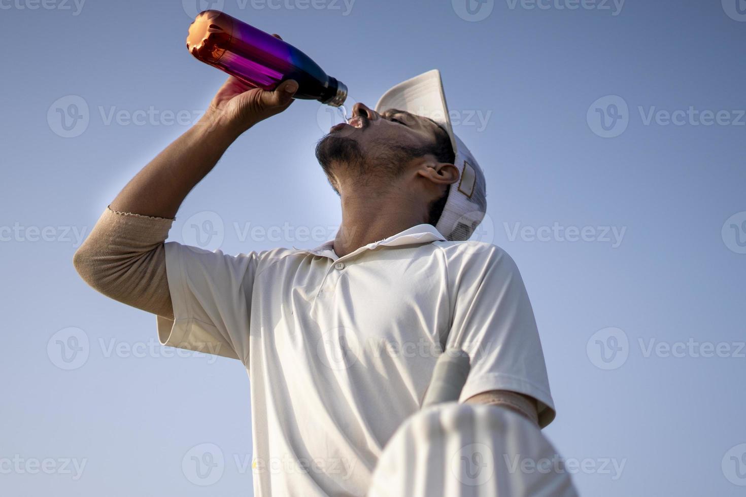 jugadores de críquet indios con vestido blanco de partidos de prueba bebiendo agua de una botella en el campo de críquet. foto
