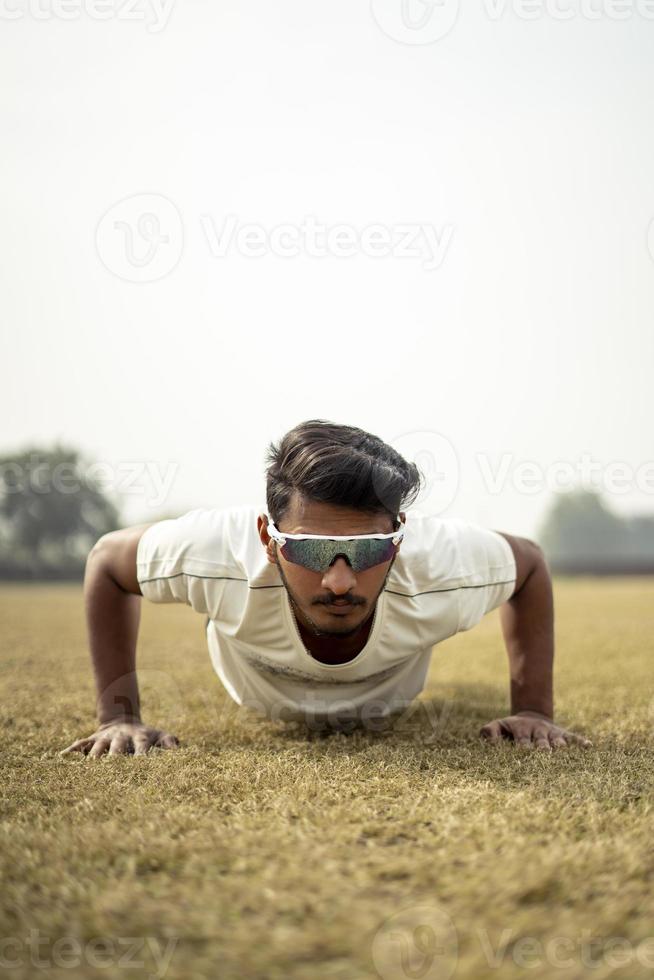 Close up portrait of a young indian sportsman exercising in the field. Sportsman doing push ups for warm up. photo