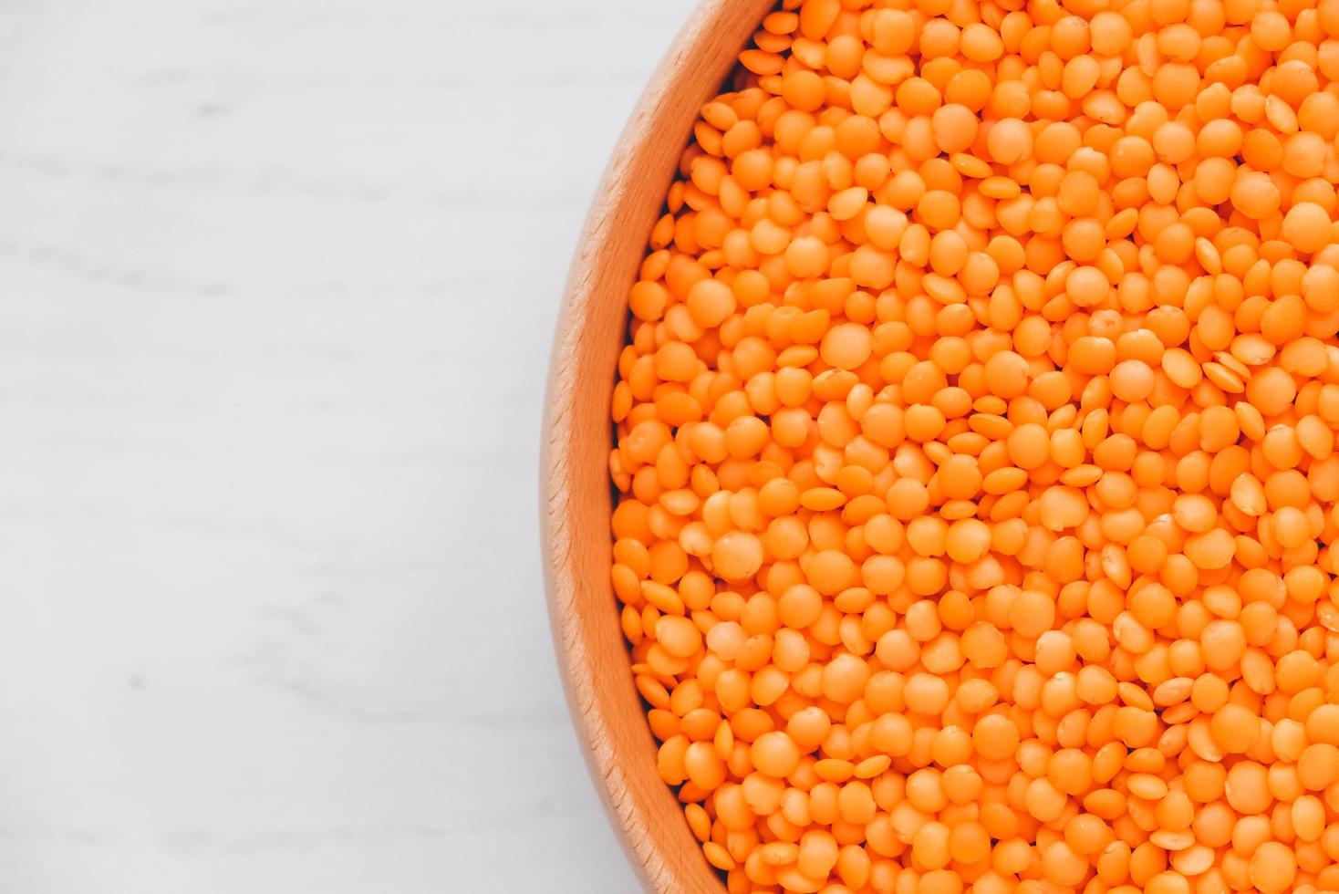 Raw red lentils in a wooden bowl on a white table photo