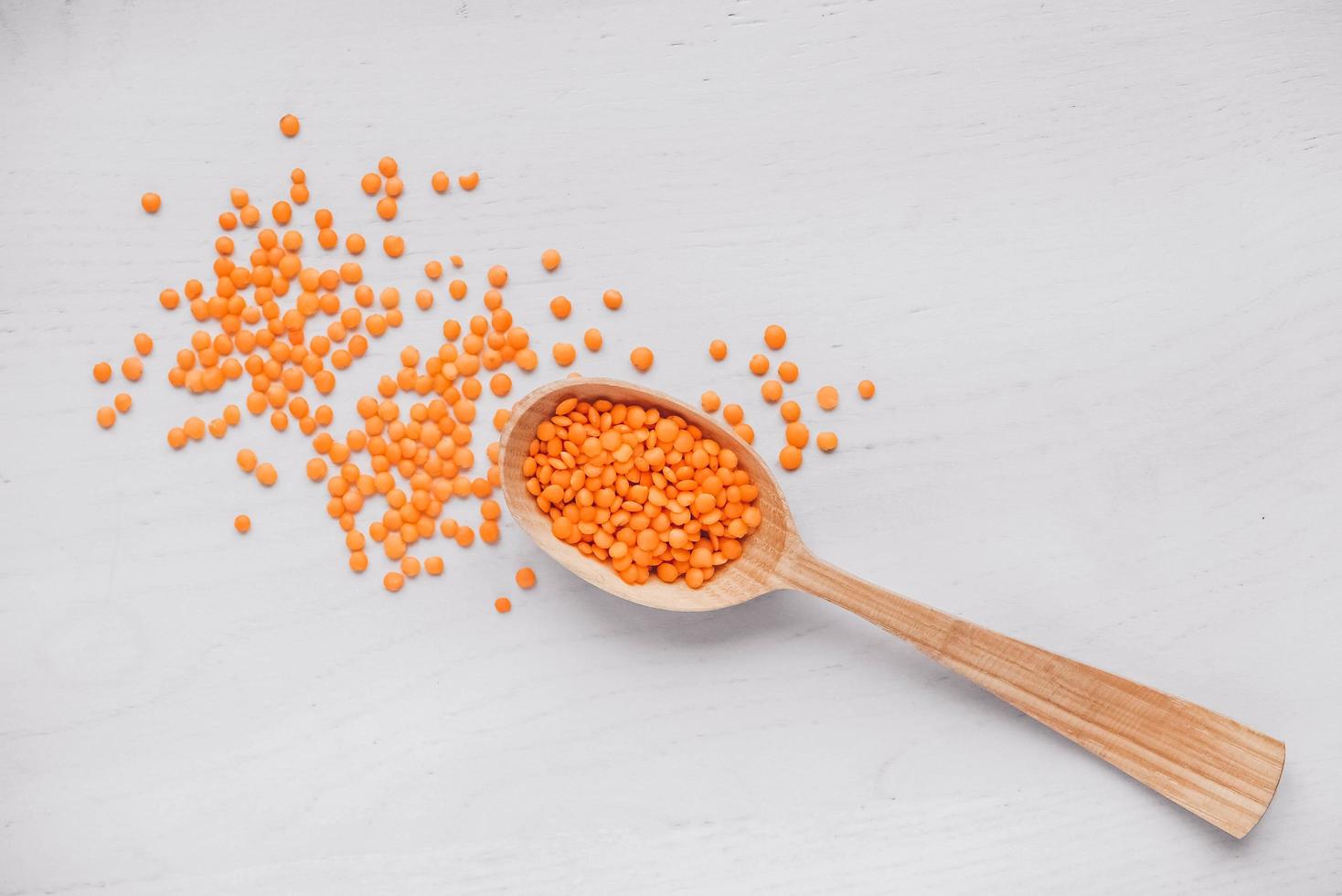 Raw red lentils in a wooden spoon on a white table photo