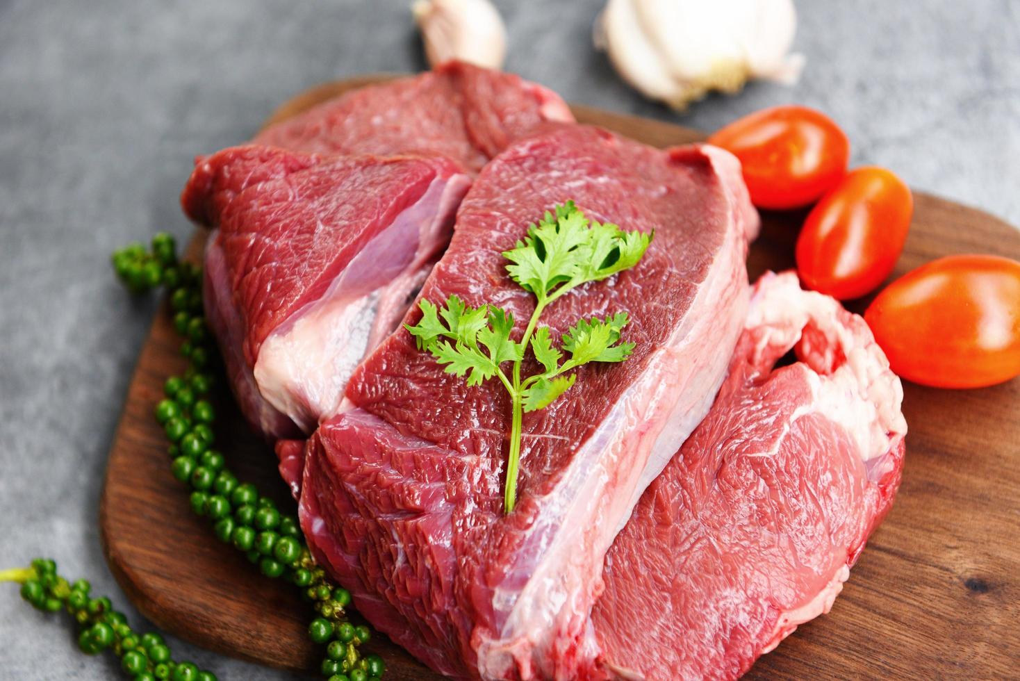 Carne de res cruda en una tabla de cortar de madera en la mesa de la cocina para cocinar bistec de ternera asado o asado a la parrilla con ingredientes hierbas y especias proteína animal de res fresca foto