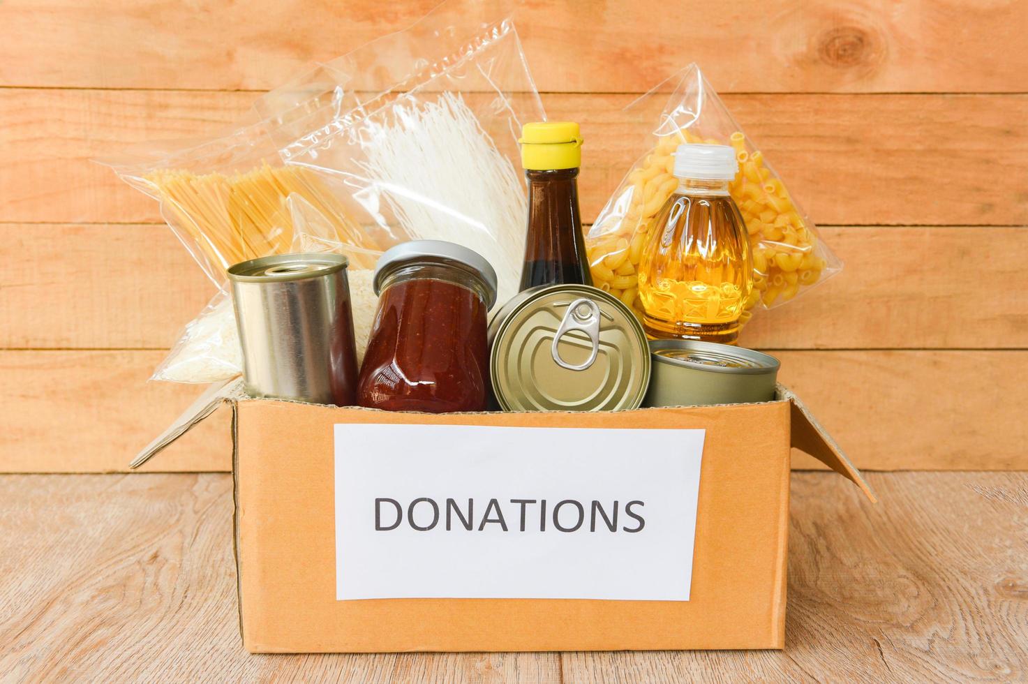 Donations box with canned food on wooden table background  pasta canned goods and dry food non perishable with cooking oil rice noodles spaghetti macaroni donations food photo